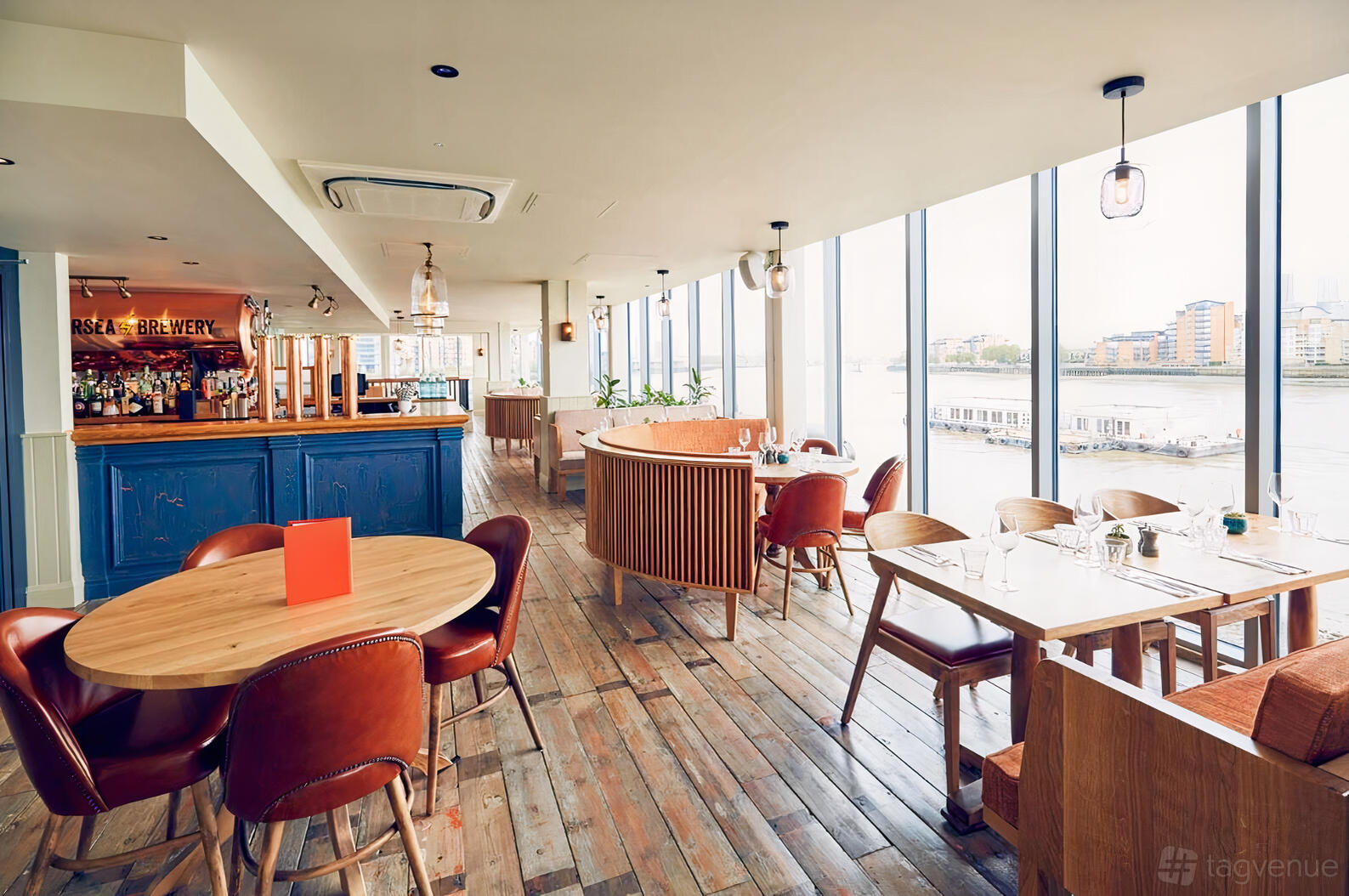 A riverside pub interior with floor-to-ceiling windows, wooden floors, and leather chairs at The Oystercatcher.
