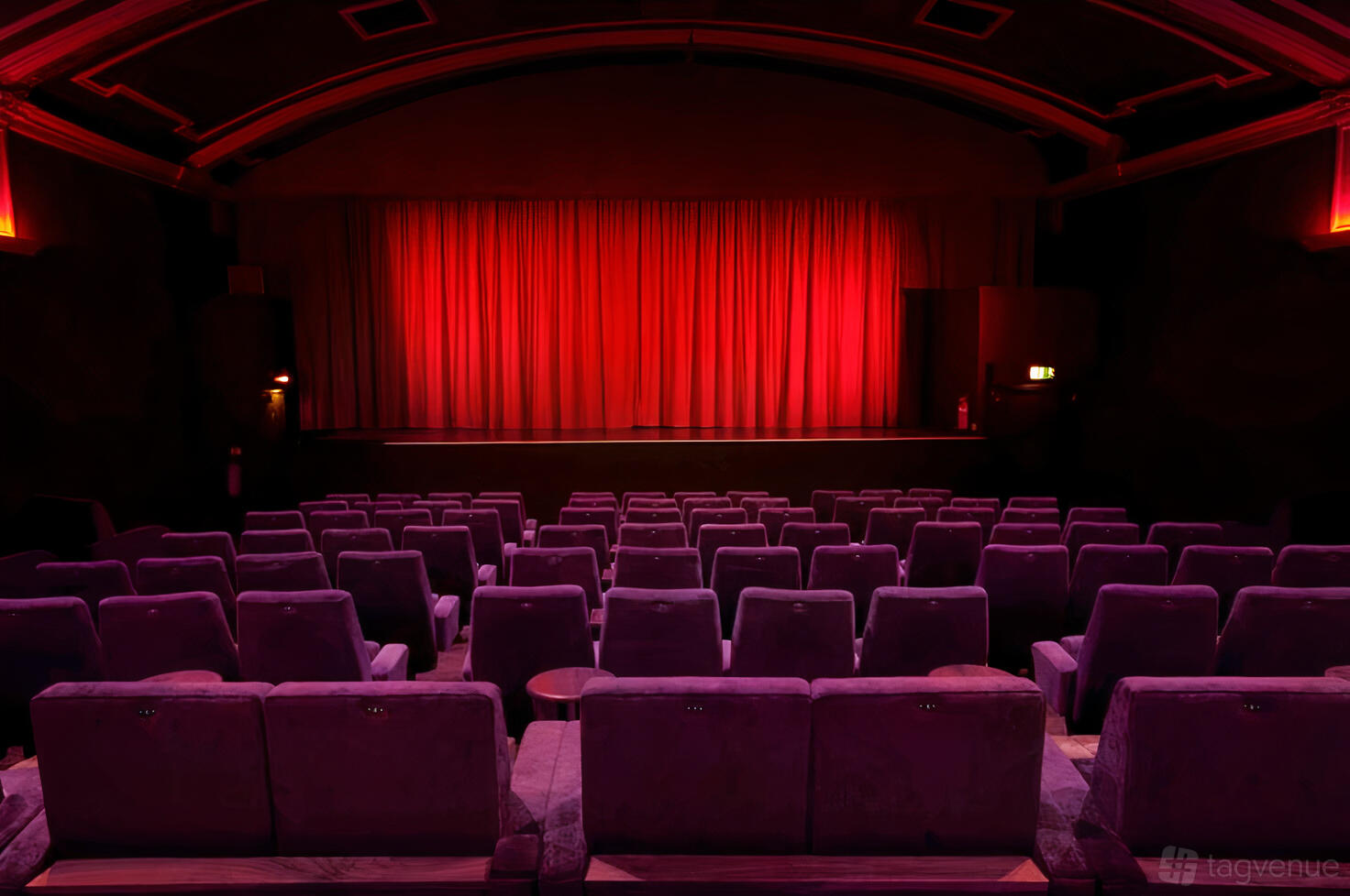 An auditorium with plush theater seating and a red-lit stage with closed curtains at Everyman Screen on the Green.