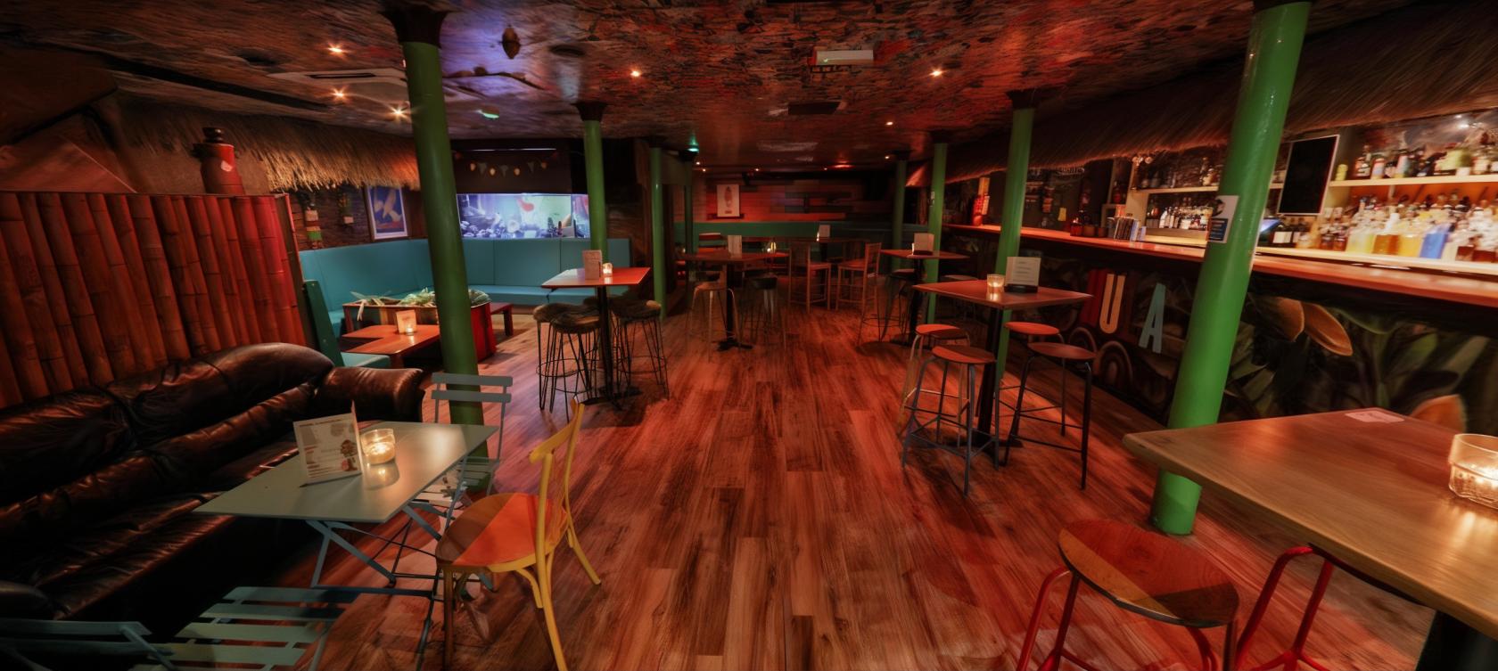 A bar with wooden floors, colorful stools, tiki-style decor, and candlelit tables at The Hula Manchester.