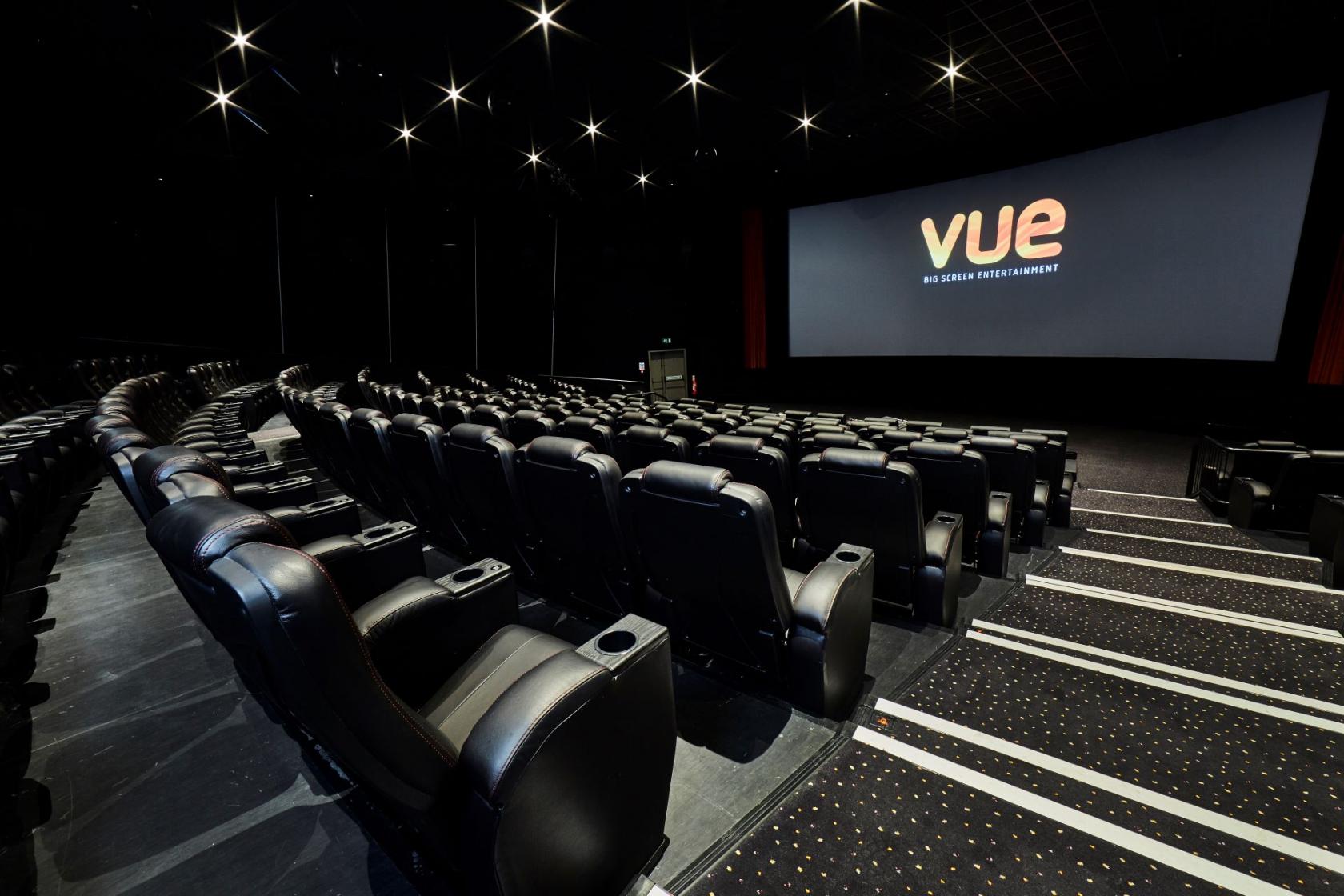 A cinema screening room with tiered rows of black leather seats facing a large projection screen at Vue West End.