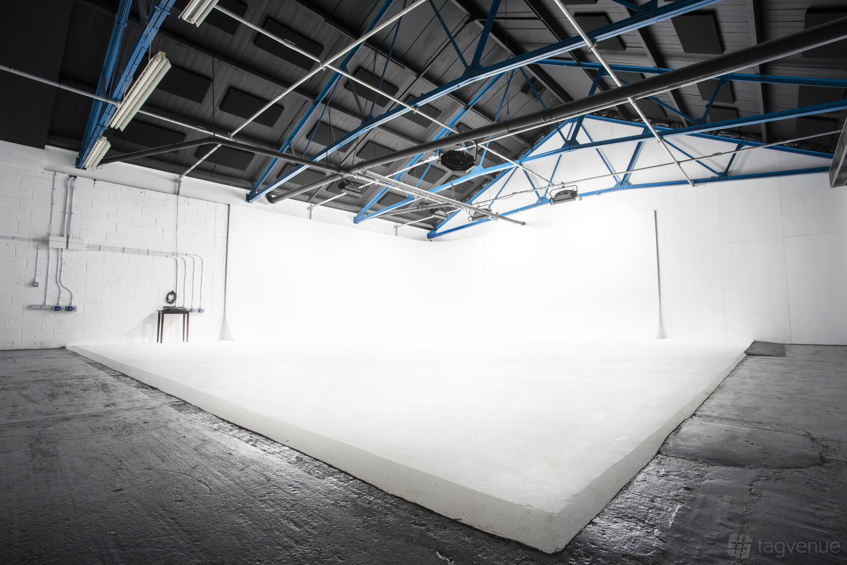 A photo studio with a large white infinity cove, exposed ceiling beams, and concrete floors at Drive-in Infinity Cove.