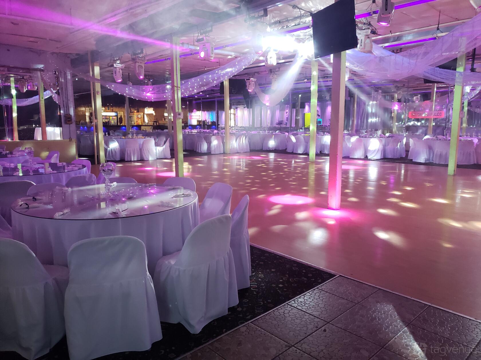 A spacious hall with round tables draped in white linens and a large open dance floor at Salon Acapulco Banquet Hall.