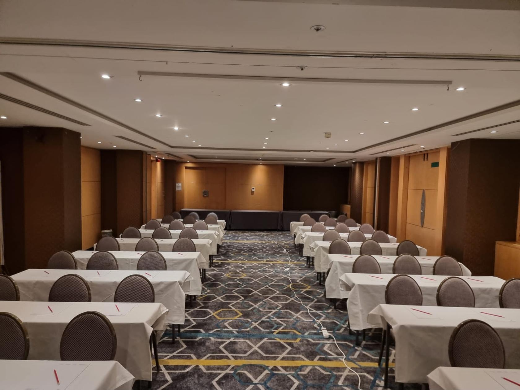 An event space with rows of round-backed chairs and white-covered tables facing a stage at Courthouse Hotel Soho.