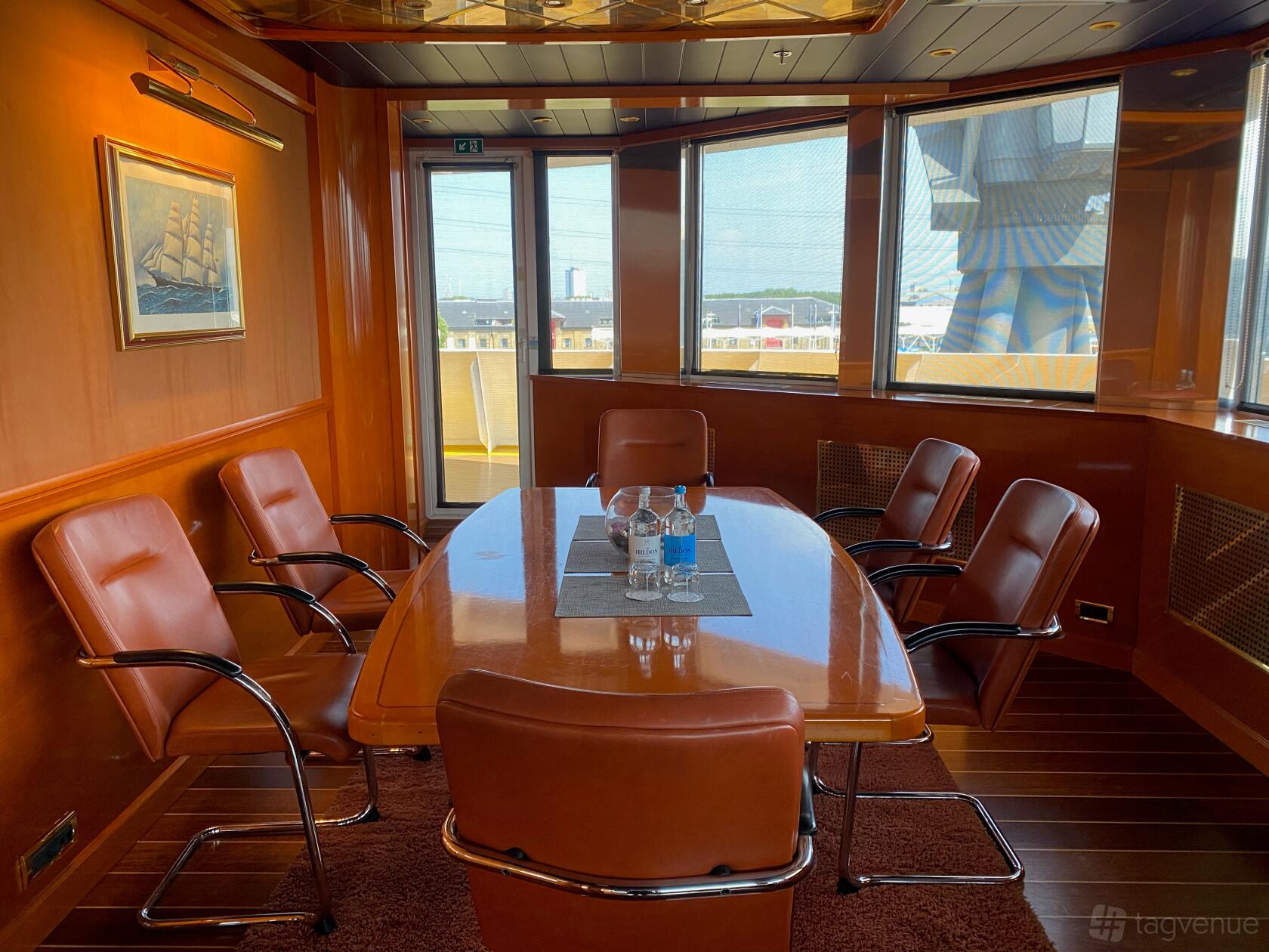 A meeting room with wood-paneled walls, leather chairs, and glass doors at Sunborn London Yacht Hotel.