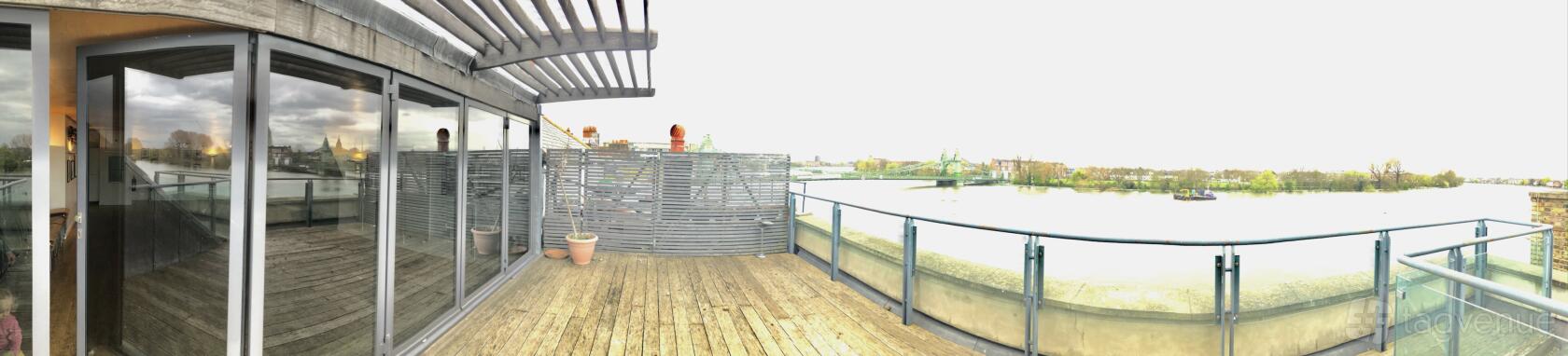 A rooftop terrace with wooden decking, glass railing, and river views at Auriol Kensington Rowing Club.