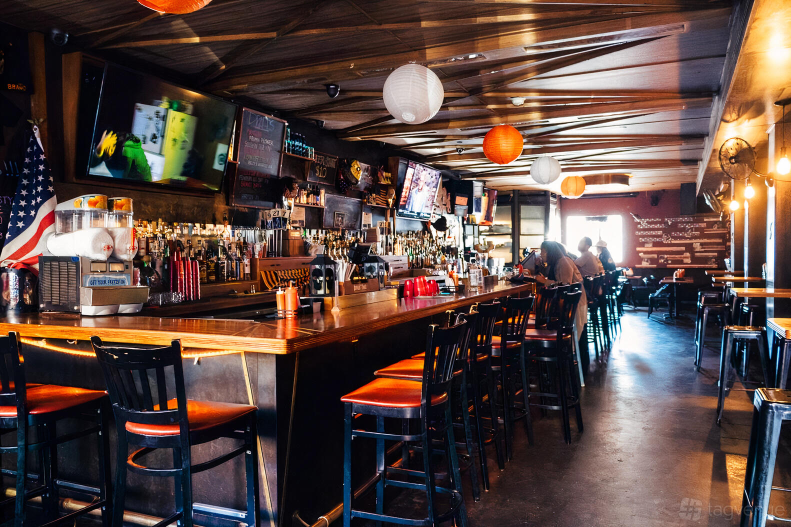 A bar with high-top stools, hanging paper lanterns, and flat-screen TVs at Kilo Bravo.