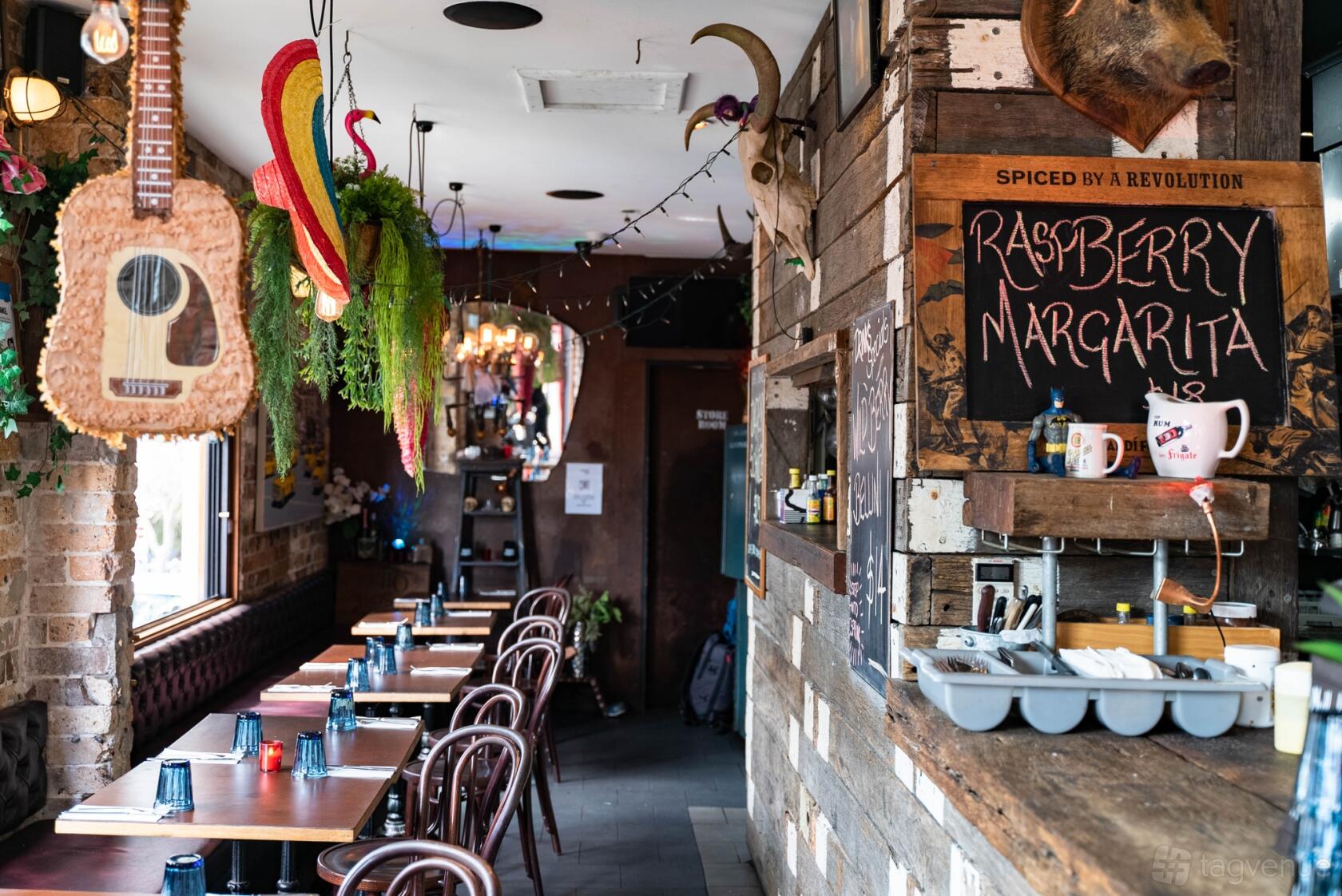 A bar with rustic wood accents, hanging plants, eclectic decor, and a row of tables at Corner Bar Rozelle.