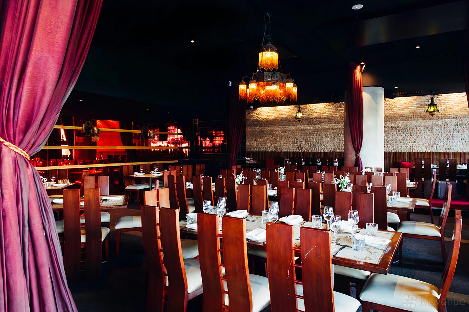 A dining room with wooden chairs, set tables, purple drapes, and hanging lanterns at Byblos Bar and Restaurant.