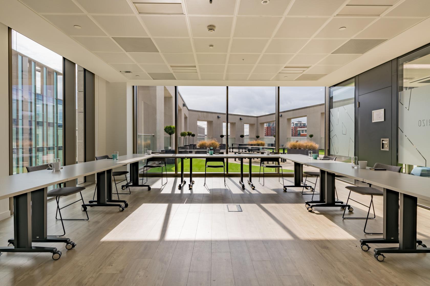 A meeting room with floor-to-ceiling windows, U-shaped tables, and courtyard views at The Terrace.