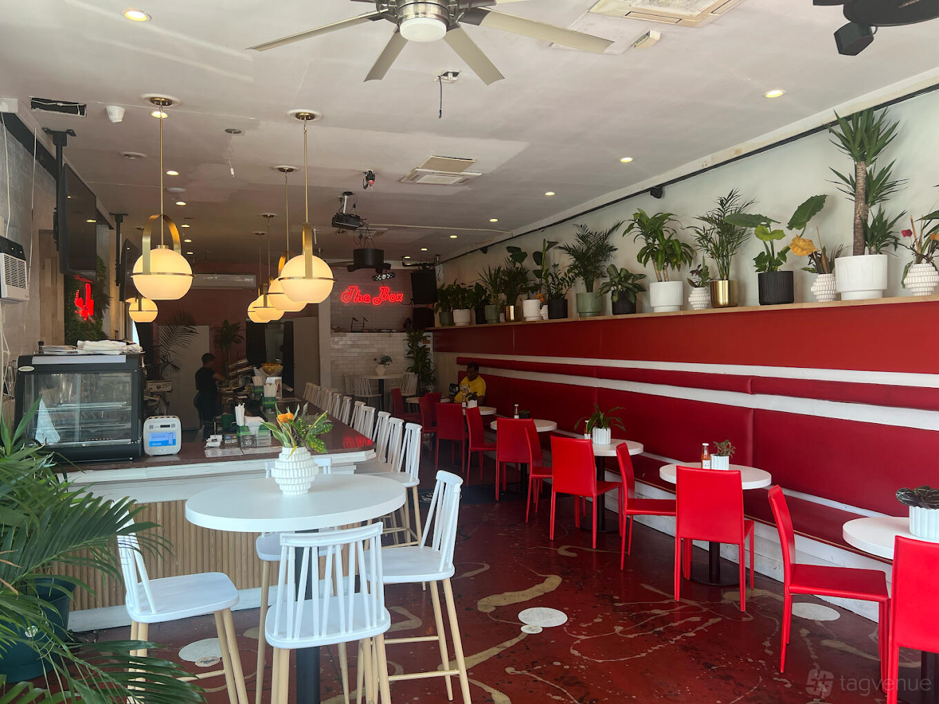 A bar with red and white decor, round tables, pendant lights, and potted plants at The Juicy Box Bar.