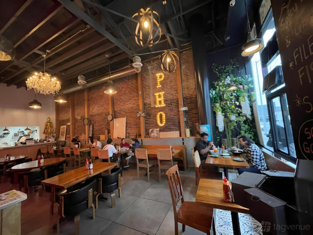 A restaurant with exposed brick walls, high ceilings, and neon PHO sign at The Sisters Café Vietnamese & Asian Fusion.
