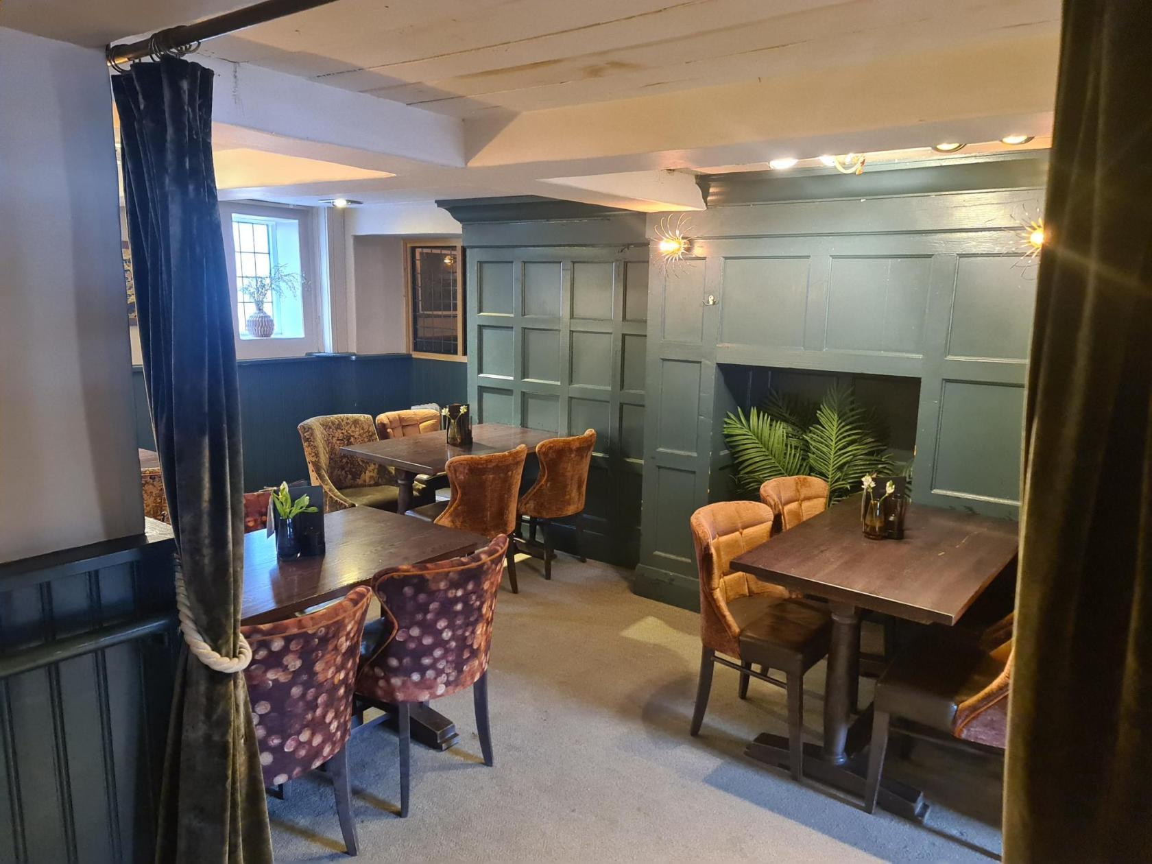 A dining room in a pub with wood-paneled walls, patterned upholstered chairs, and potted plants at Seahorse.
