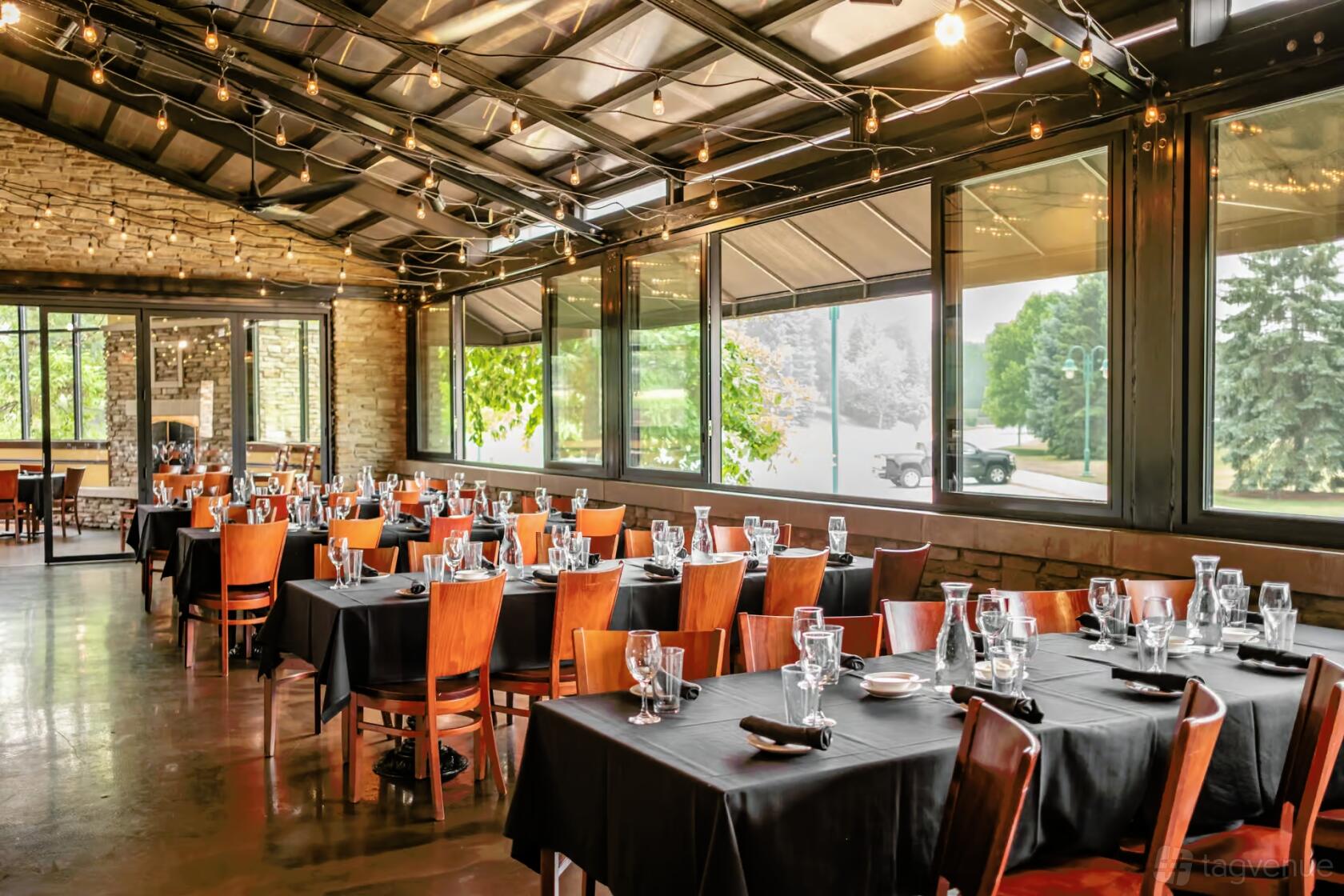 A dining room with floor-to-ceiling windows, exposed stone walls, and tables with black linens at Clara's Restaurant.
