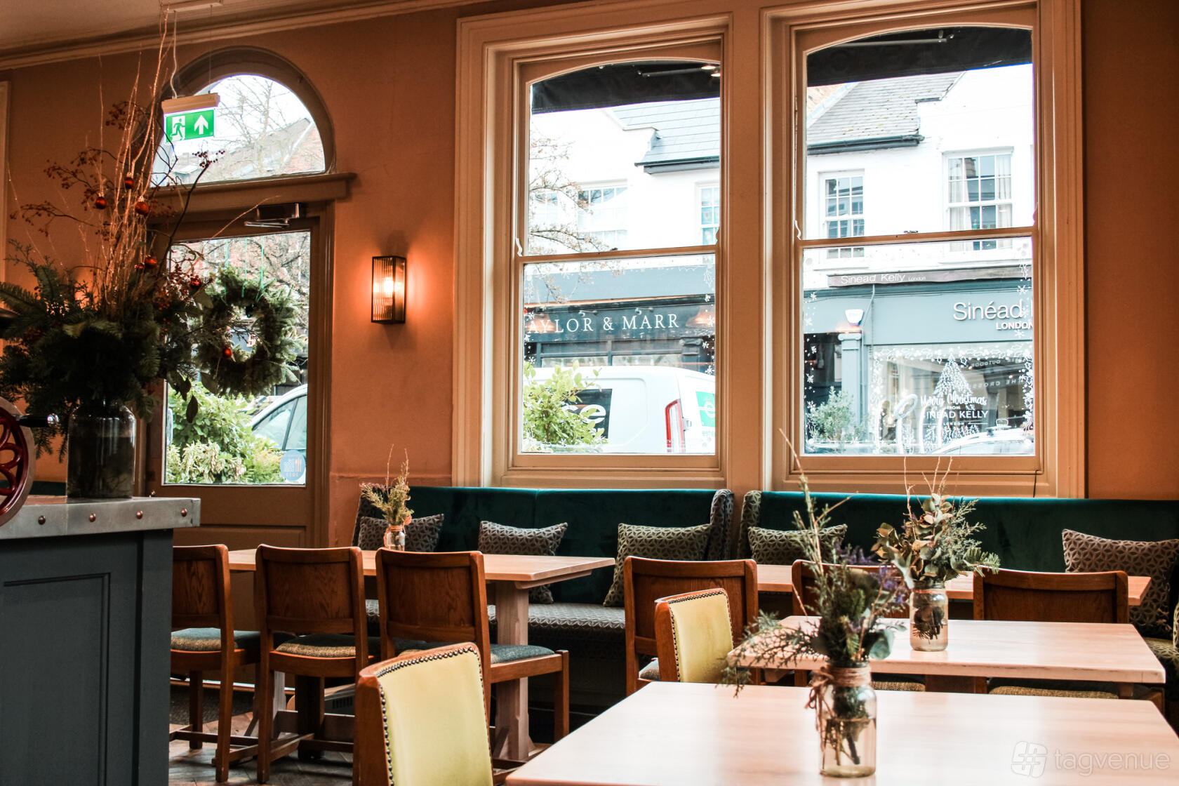 A pub with large front windows, wooden tables and chairs, and floral arrangements at The Crossing Pub.