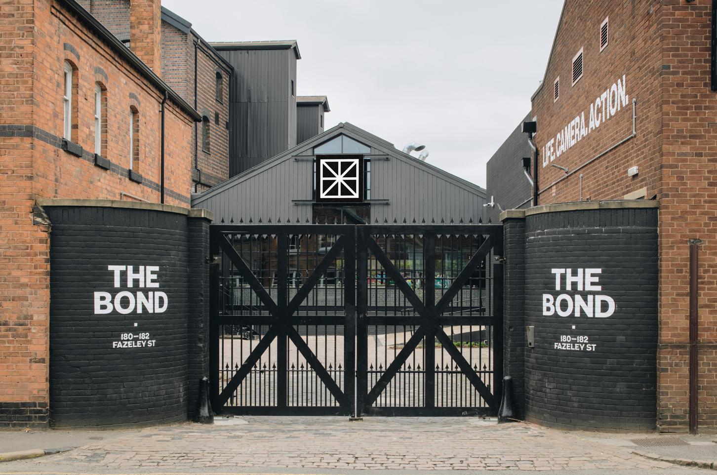 A historic building with red brick exterior, tall black gates, and industrial architectural details at The Bond.