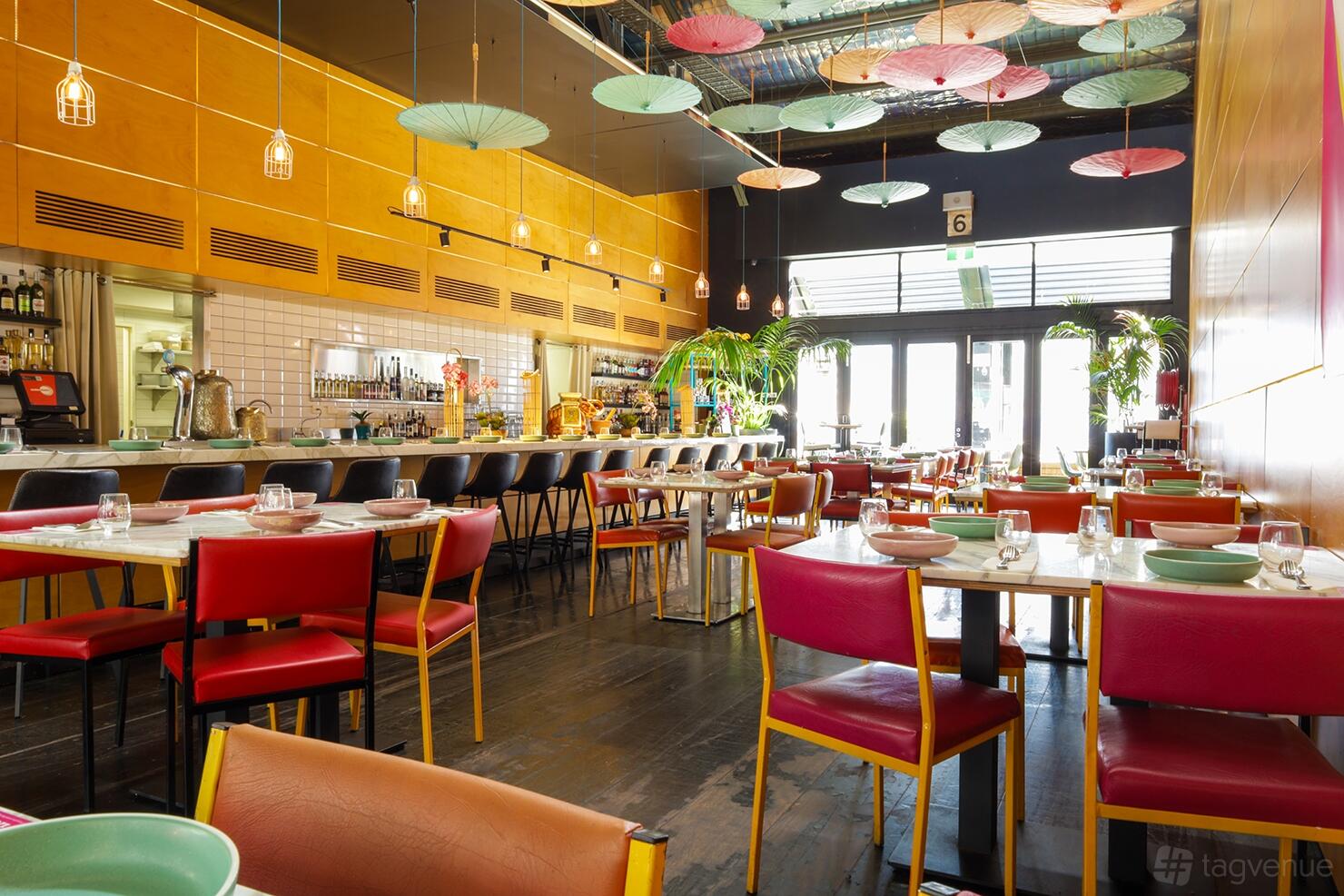A restaurant with bright chairs, parasols hanging from the ceiling, and large windows at BangPop.