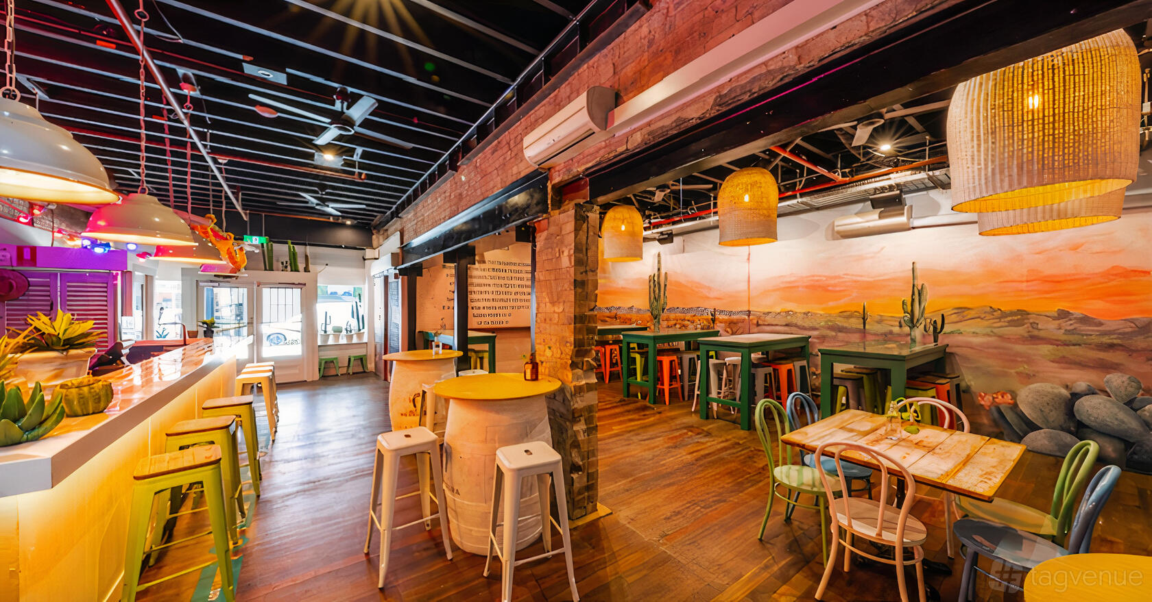 An event space in a pub with colorful stools, mural walls, exposed brick, and woven pendant lights at The Prince Consort.