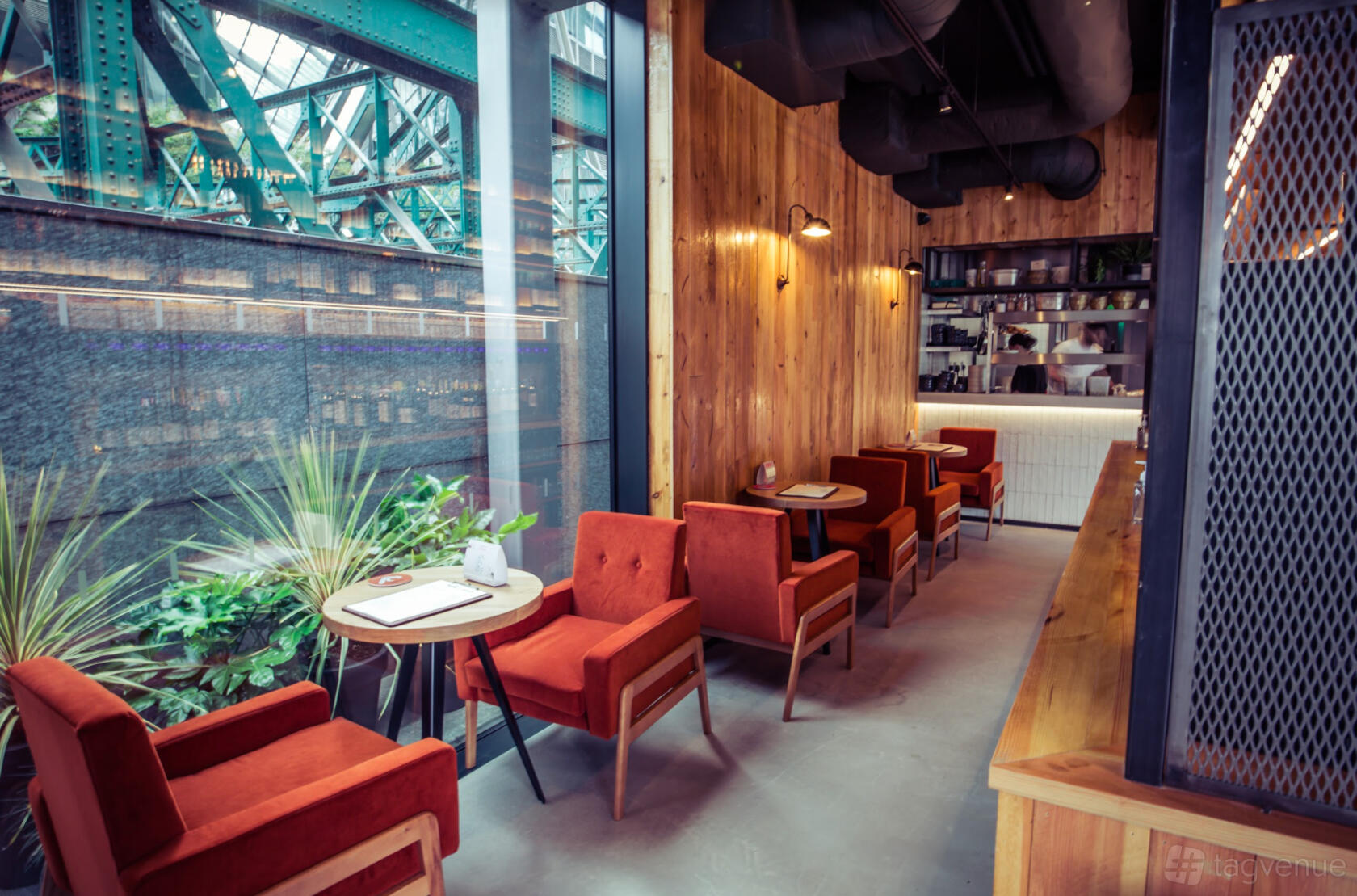 A bar with wood-paneled walls, red upholstered chairs, and floor-to-ceiling windows at Vagabond Shoreditch.
