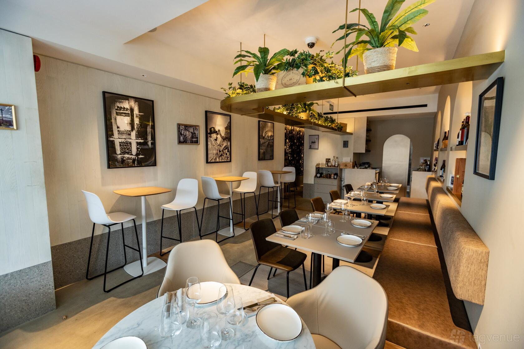 A restaurant with potted plants, wall art, marble and wooden tables, and a long upholstered bench at Apéro.