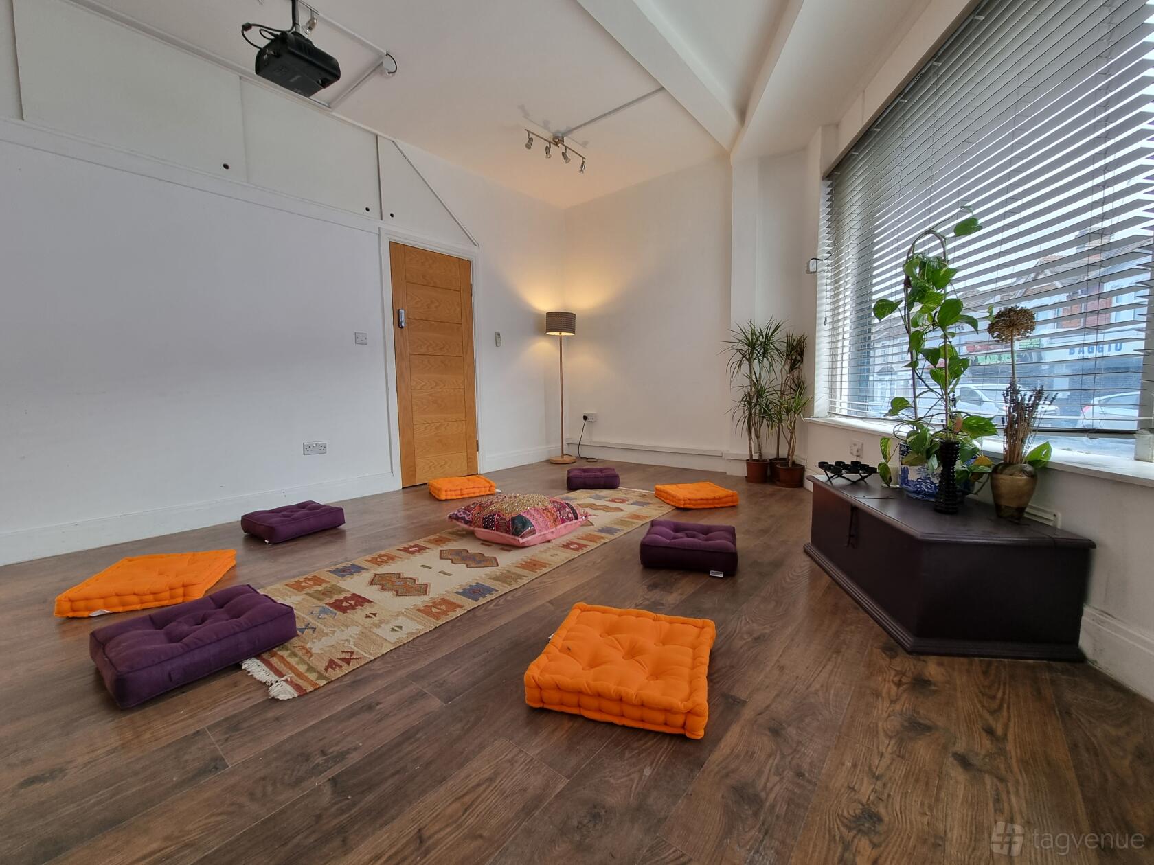 A creative space with floor cushions, a patterned rug, potted plants, and large windows at The Twelfth House.