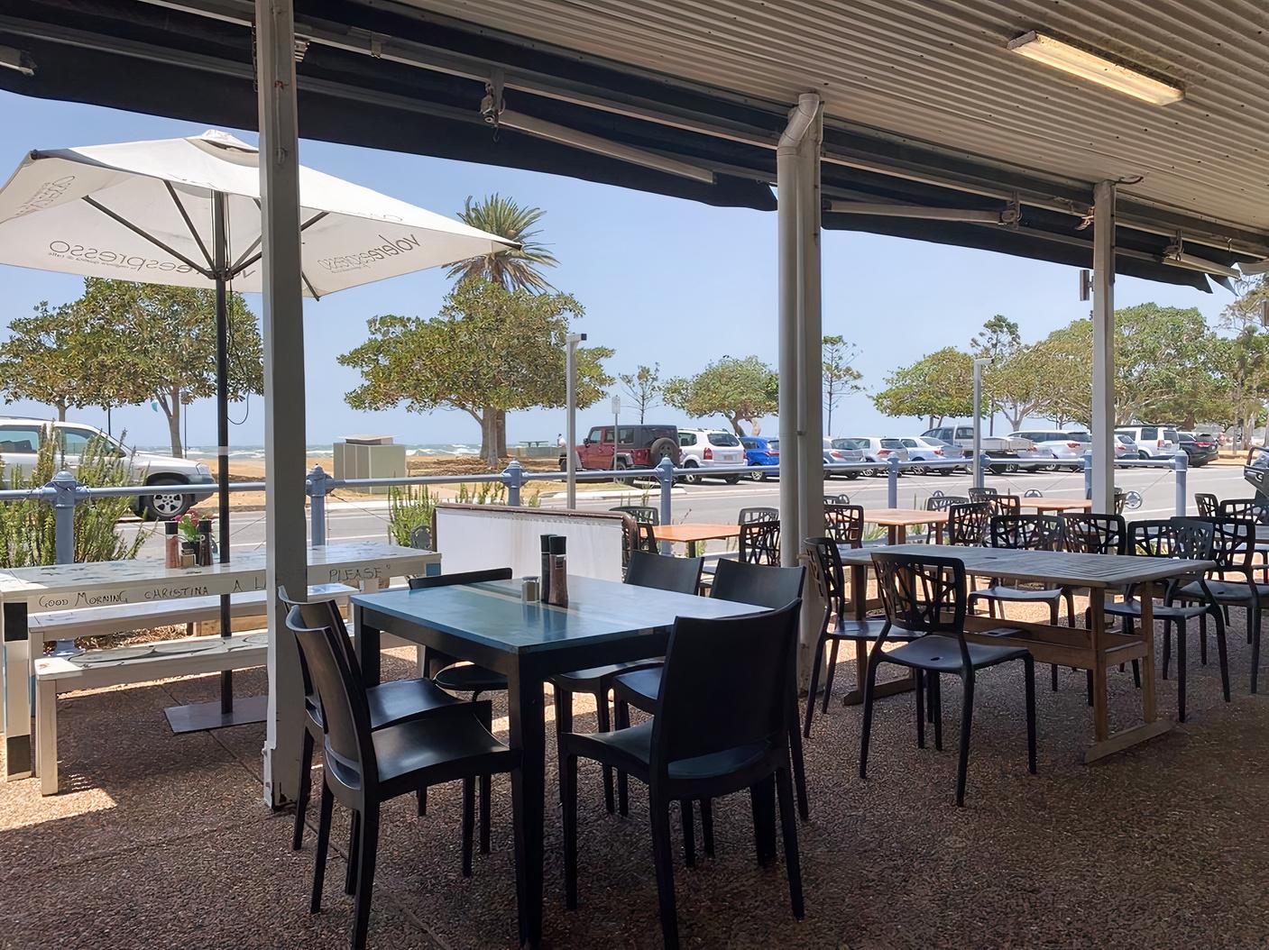 An outdoor cafe area with shaded seating, black chairs, and sea views at Baaia Cafe/Restaurant.