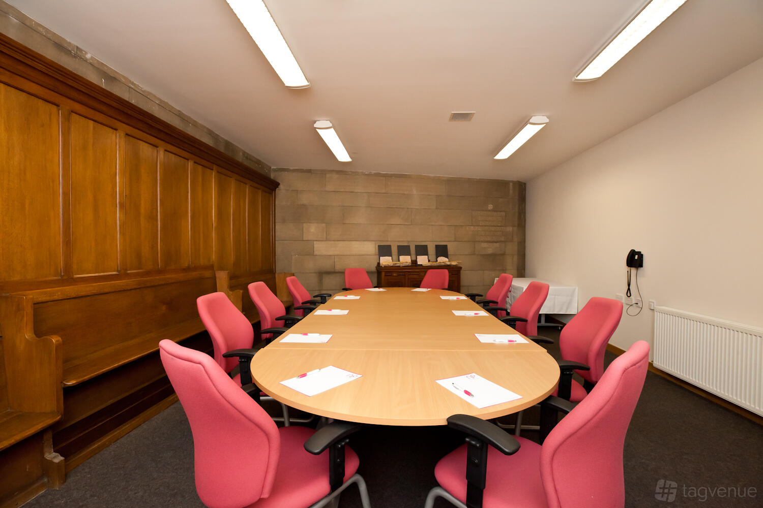 A meeting room with an oval table, pink chairs, notepads, and wood paneling at Norton Park Conference Centre.