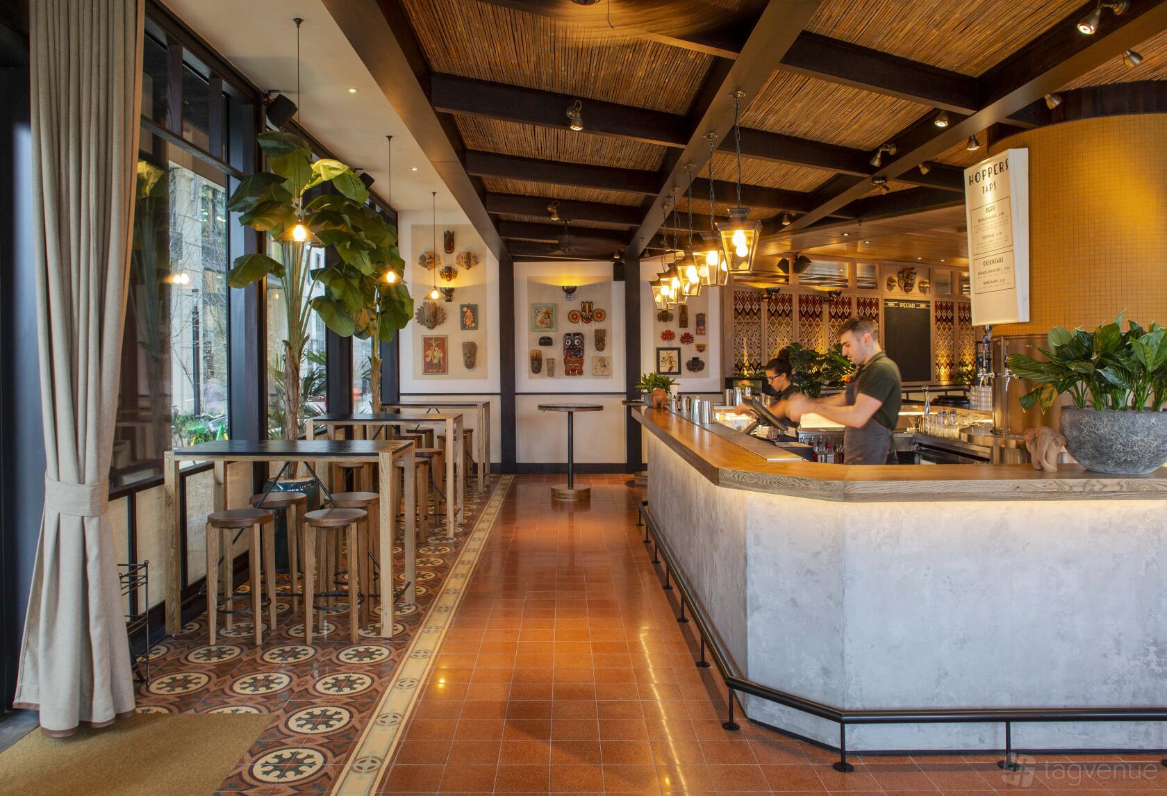 A restaurant bar with a long concrete counter, pendant lights, patterned tile floor, and tall windows at Hoppers King's Cross.