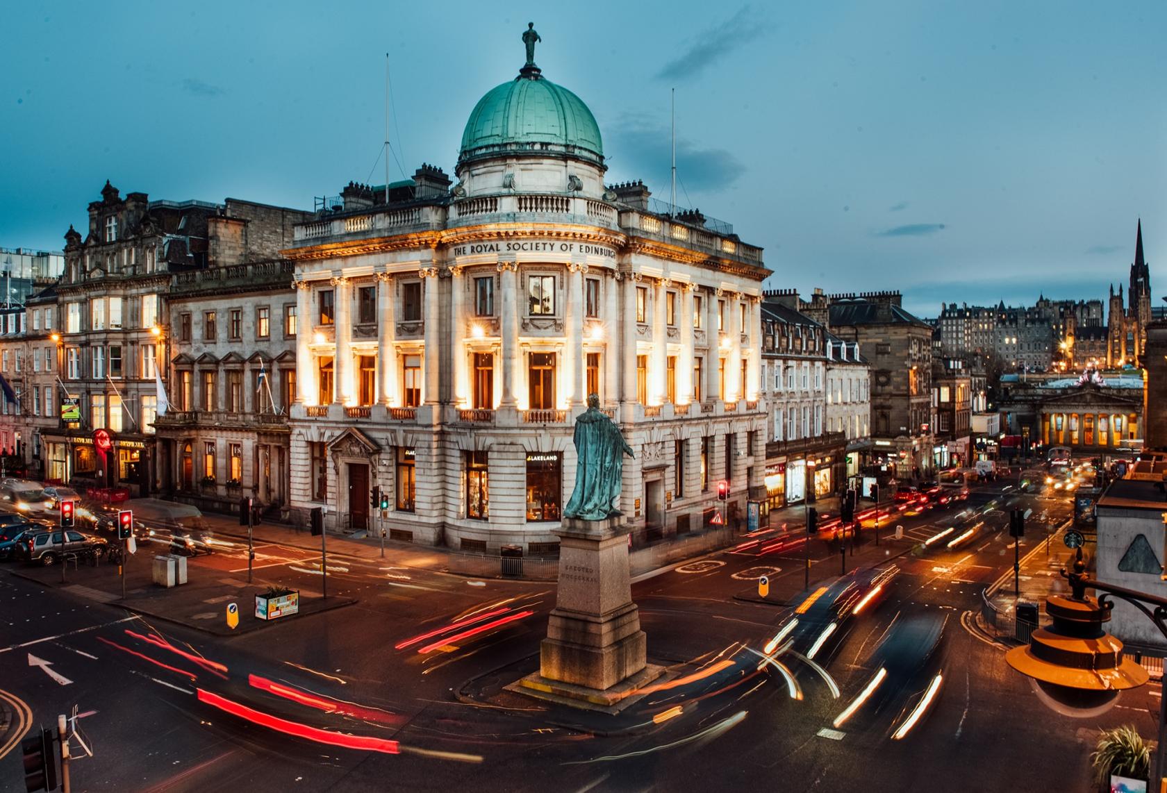 A historic conference centre with a domed roof and illuminated façade on a busy street at The Royal Society of Edinburgh.