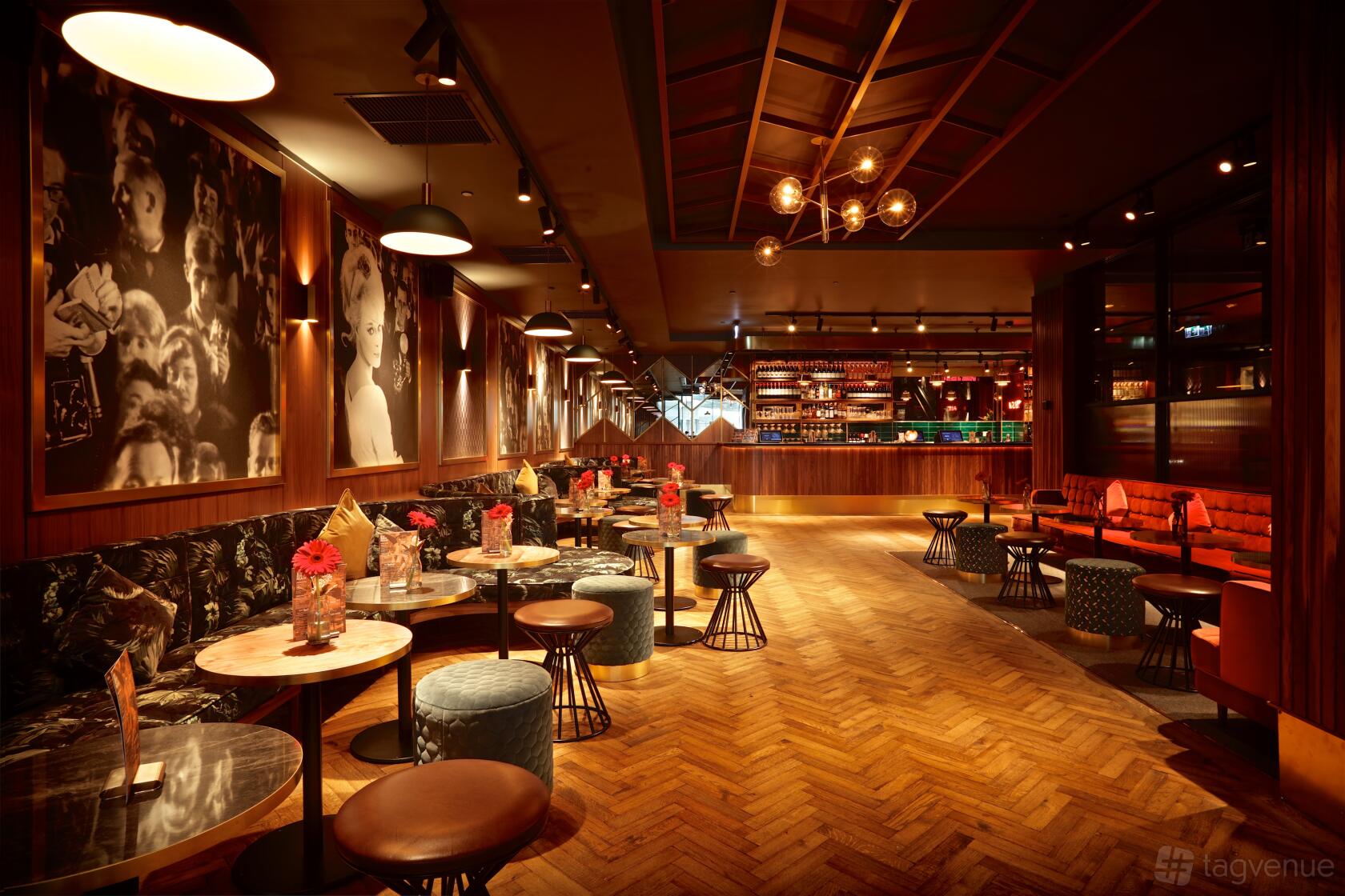 A cinema lounge with marble-topped tables, velvet stools, wood flooring, and vintage movie portraits at Everyman Liverpool.