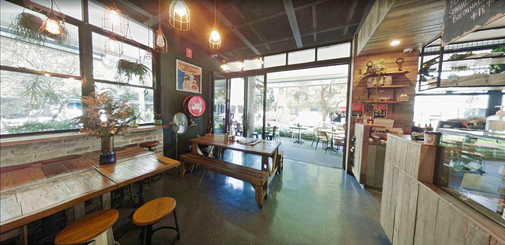 A cafe with wooden tables, hanging pendant lights, and large windows opening to an outdoor seating area at Eggspresso.