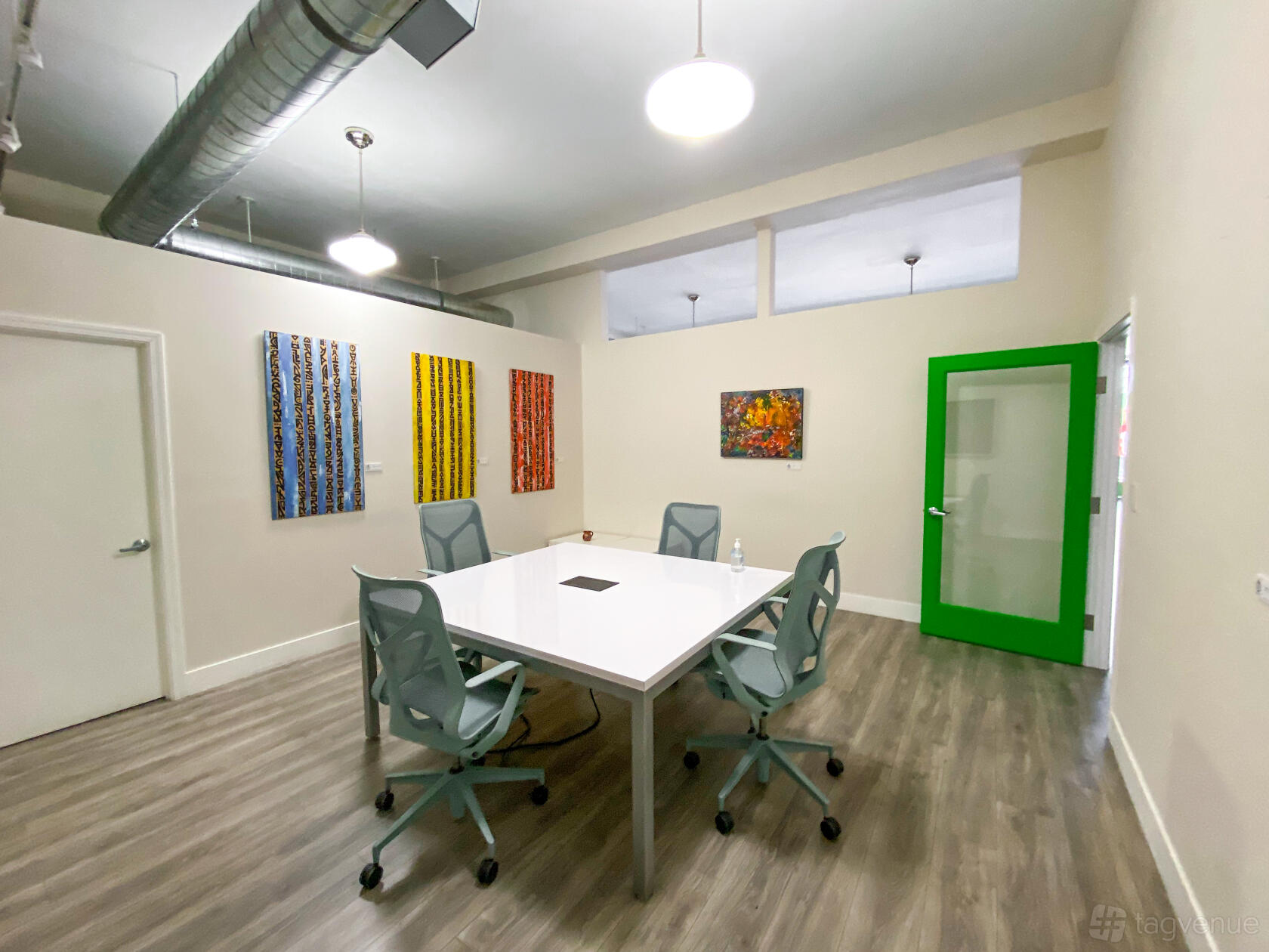 A meeting room with a white table, gray chairs, colorful abstract art, and a green-framed glass door at Oakstop 1721 Broadway.