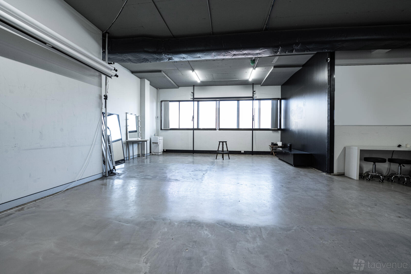 A photo studio with polished concrete floors, a makeup station, black backdrop wall, and large windows at CV Studios.