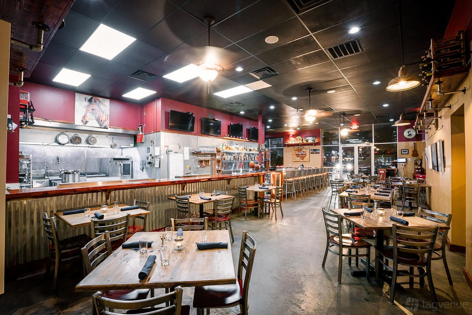 An event space in a restaurant with wooden tables, exposed kitchen, and mounted TVs at Hops and Thyme.