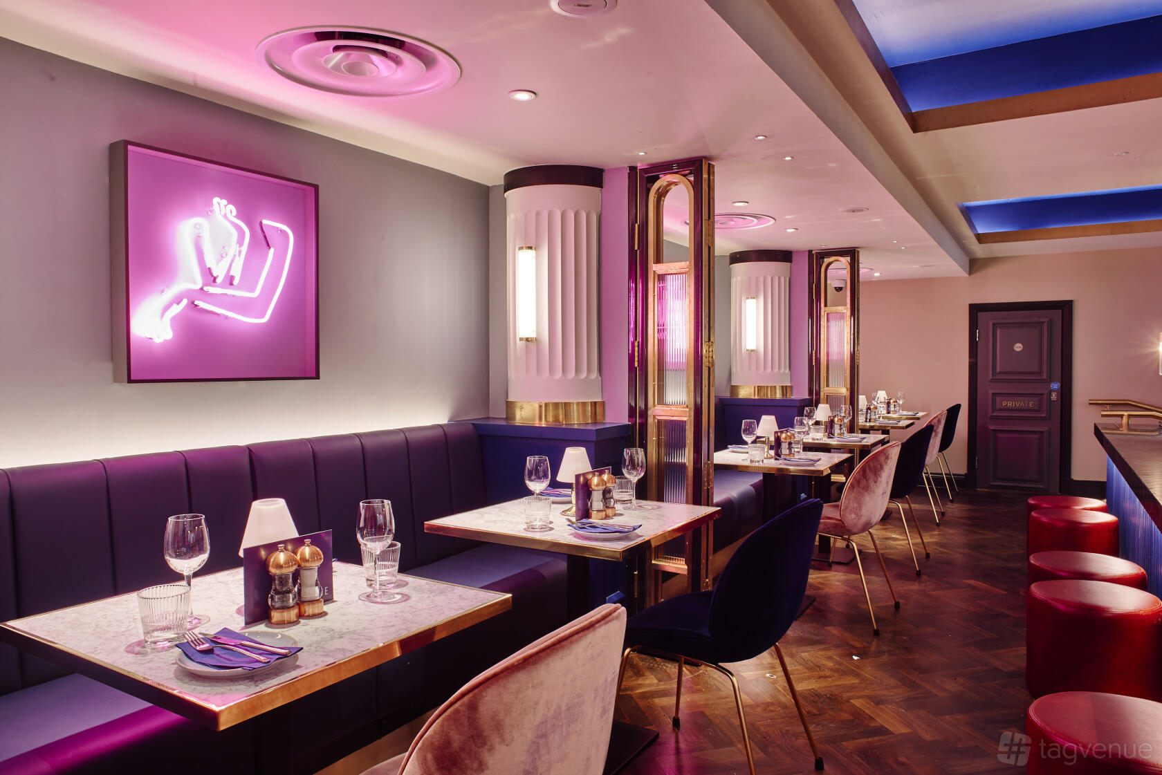 An event space with marble tables, velvet seating, neon wall art, and ambient pink lighting at Le Monde Hotel.
