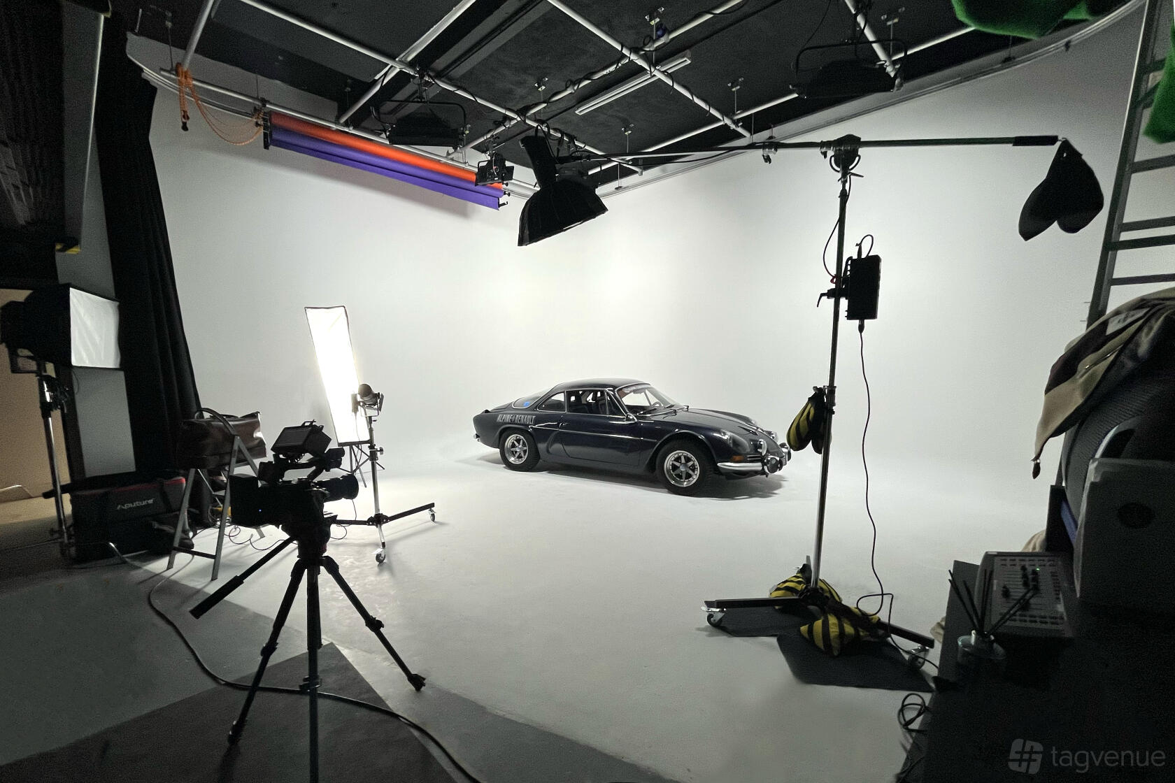 A photo and film studio with a white cyclorama wall, vintage car, tripods, and studio lighting at Aquifer Film Studio.