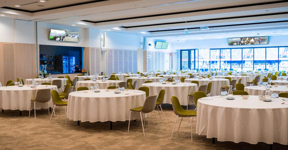 An event space with round tables covered in white linens, green chairs, and large windows at CommBank Stadium.