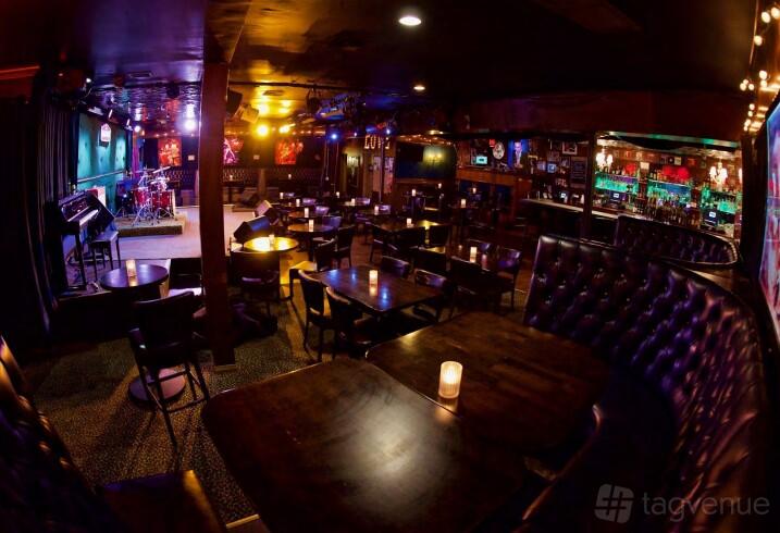 A nightclub with tufted leather booths, round tables, a stage for live music, and colored lighting at The Mint.