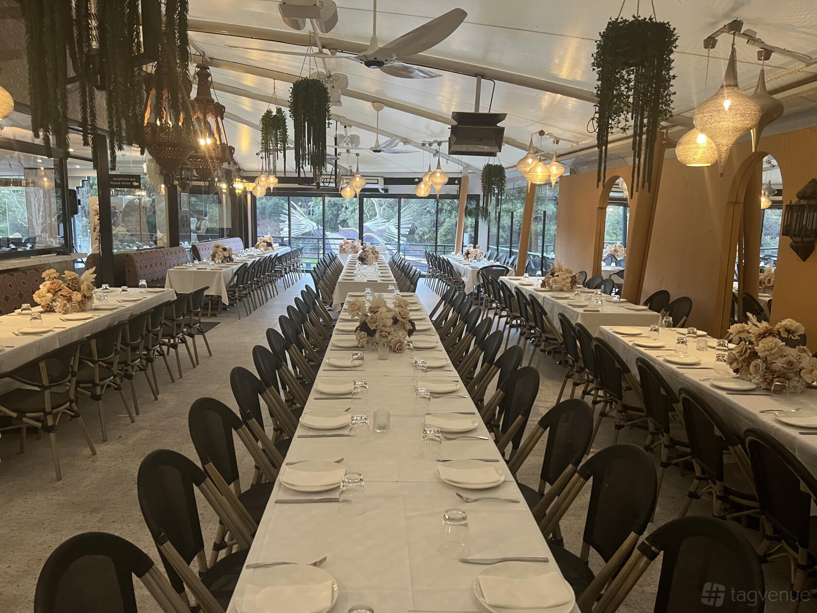 An alfresco dining terrace with long banquet tables, hanging pendant lights, and greenery at Sahra By The River.