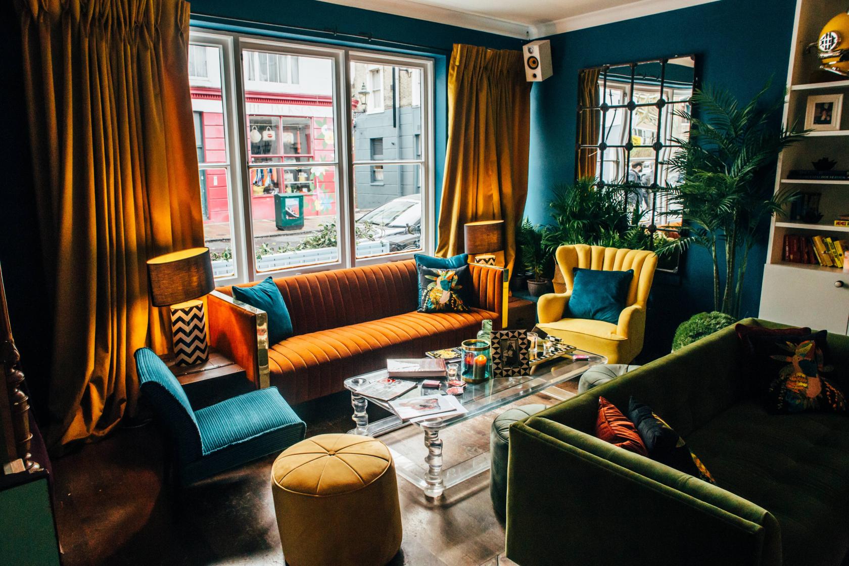A cocktail bar with colorful velvet armchairs, a glass coffee table, and large windows at The Little Yellow Door.