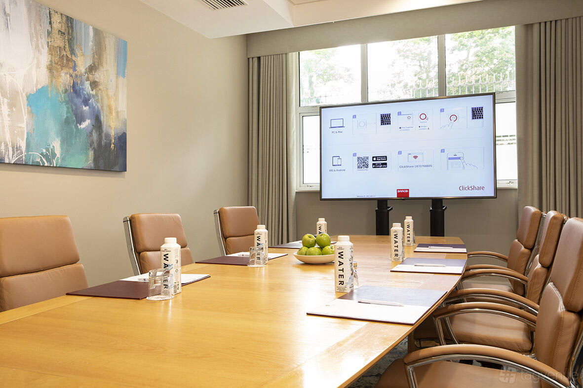 A hotel meeting room with tan leather chairs, a wooden conference table, and a presentation screen at Grand Hotel.