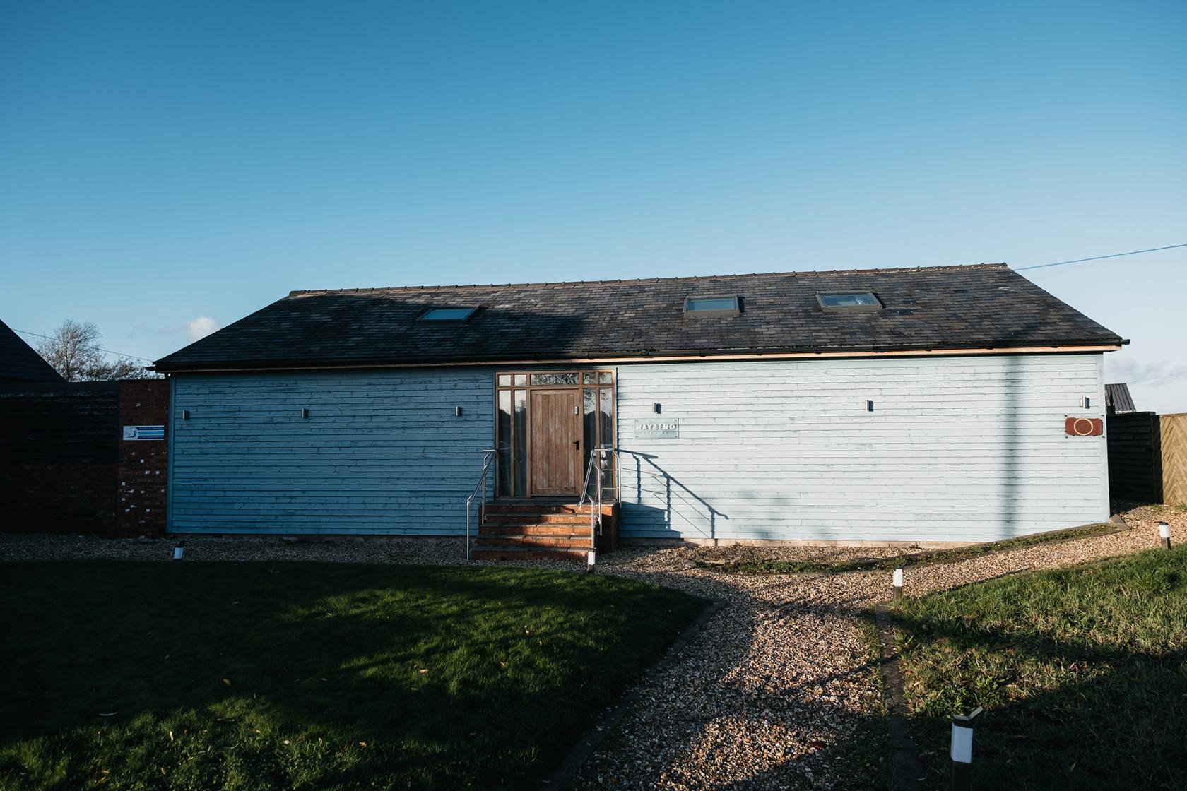 A blank canvas venue with light blue wooden exterior walls, a central wooden door, and stone steps at HAYBENO Studios.