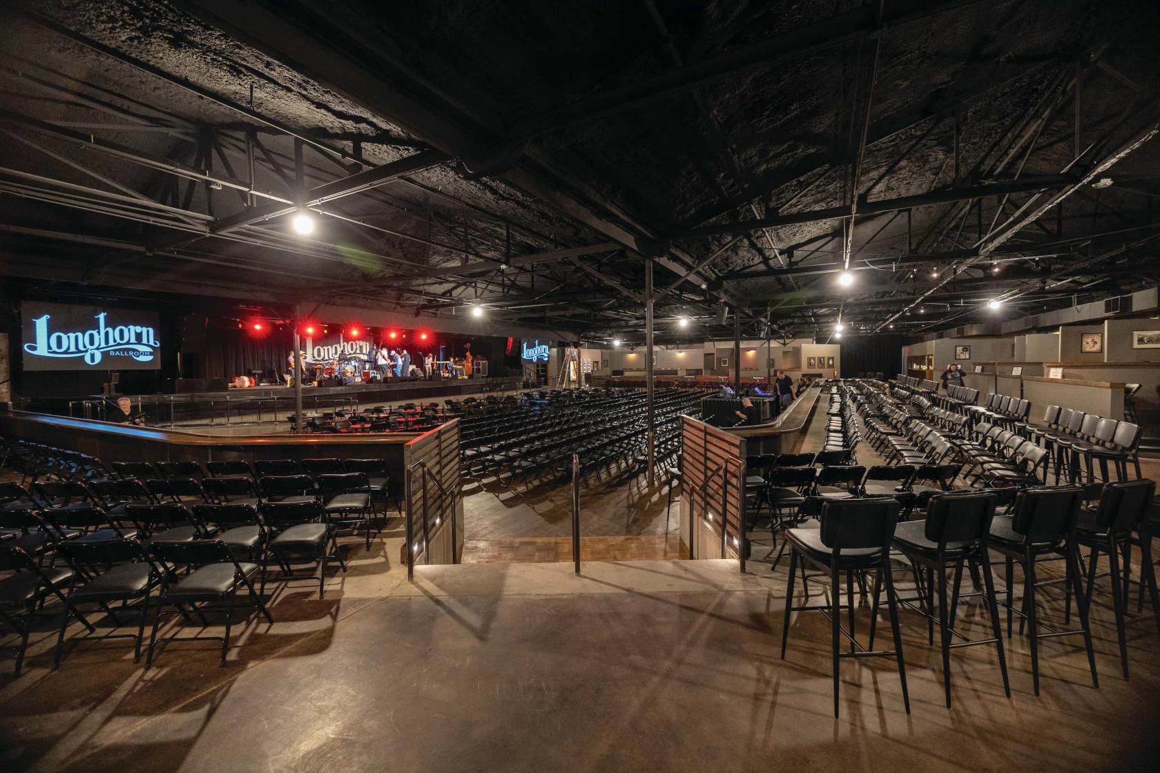 An event venue with a stage, rows of black chairs, and tiered seating at Longhorn Ballroom.