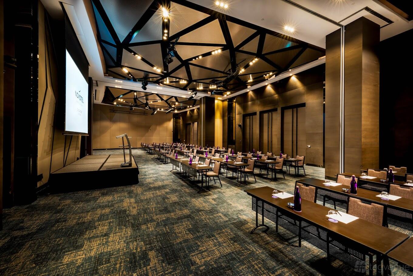 A hotel banqueting hall with exposed ceiling beams, stage, and rows of tables set for a meeting at Novotel Singapore on Stevens.