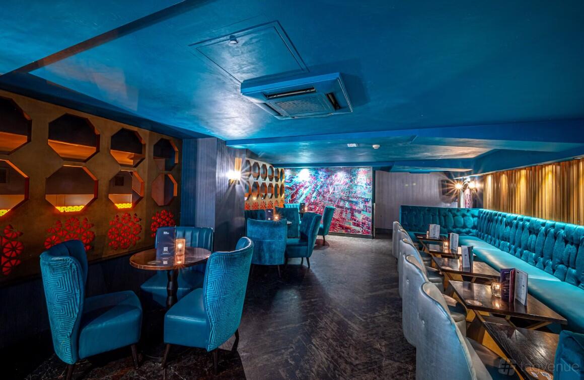 A function room in a cocktail bar with plush blue seating, honeycomb wall panels, and colorful mural at Dirty Martini St. Paul's.