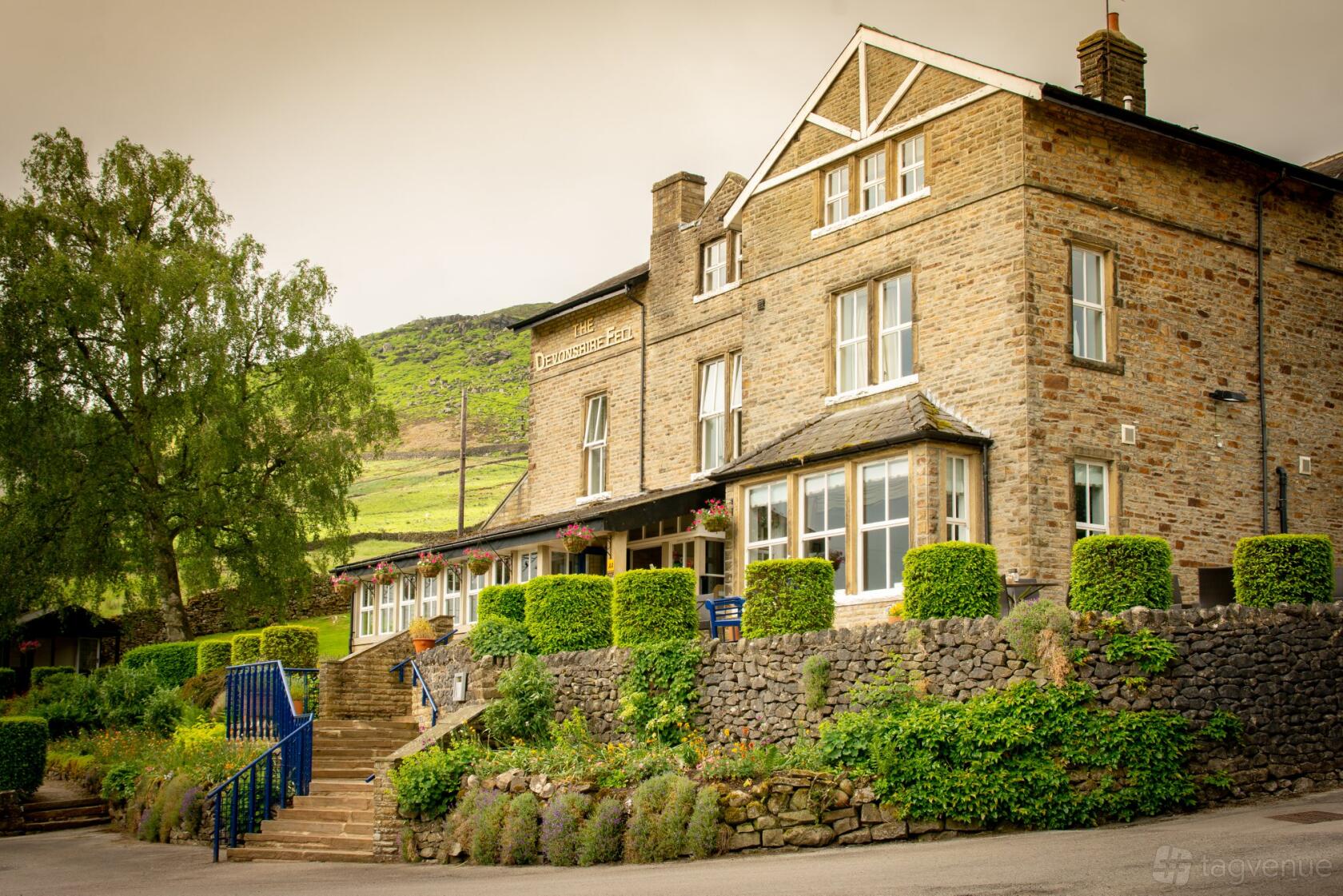A stone hotel with large windows, manicured hedges, and hillside views at The Devonshire Fell Hotel & Restaurant.
