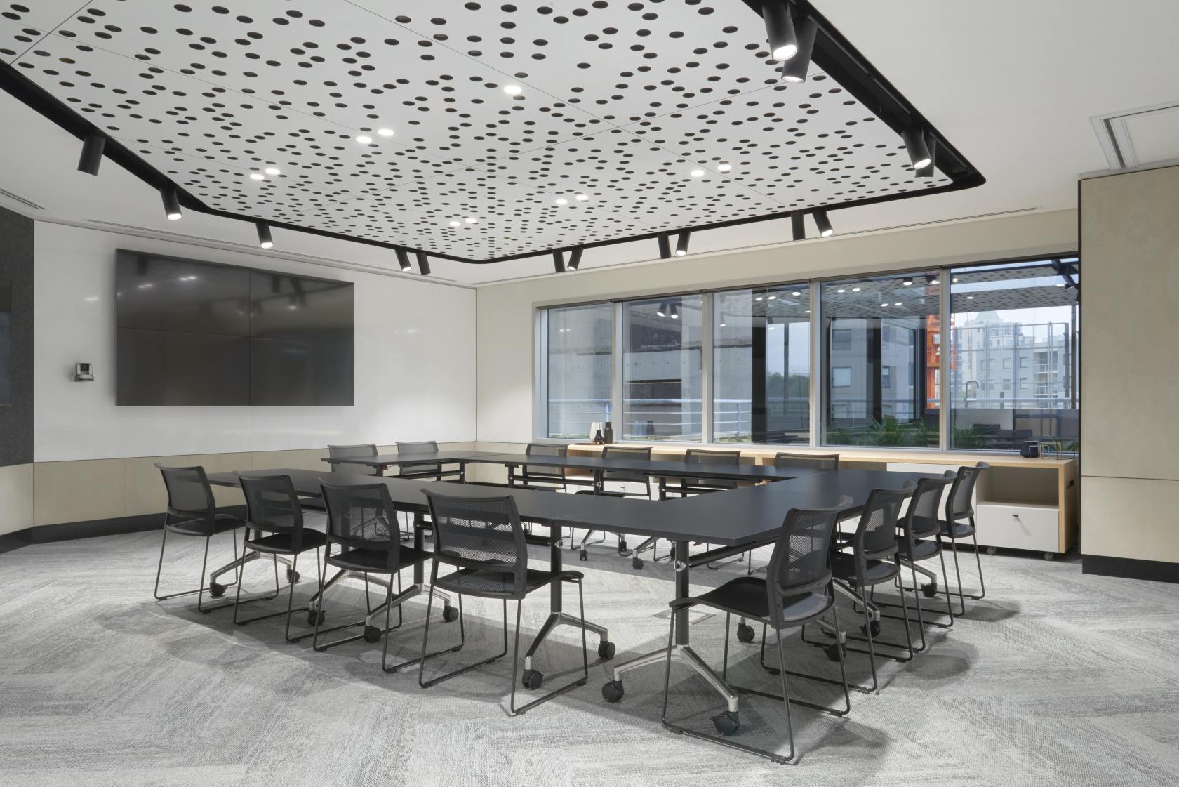 A meeting room with a U-shaped table setup, black chairs, large windows, and a dotted acoustic ceiling at Flex by ISPT at Spring Place.