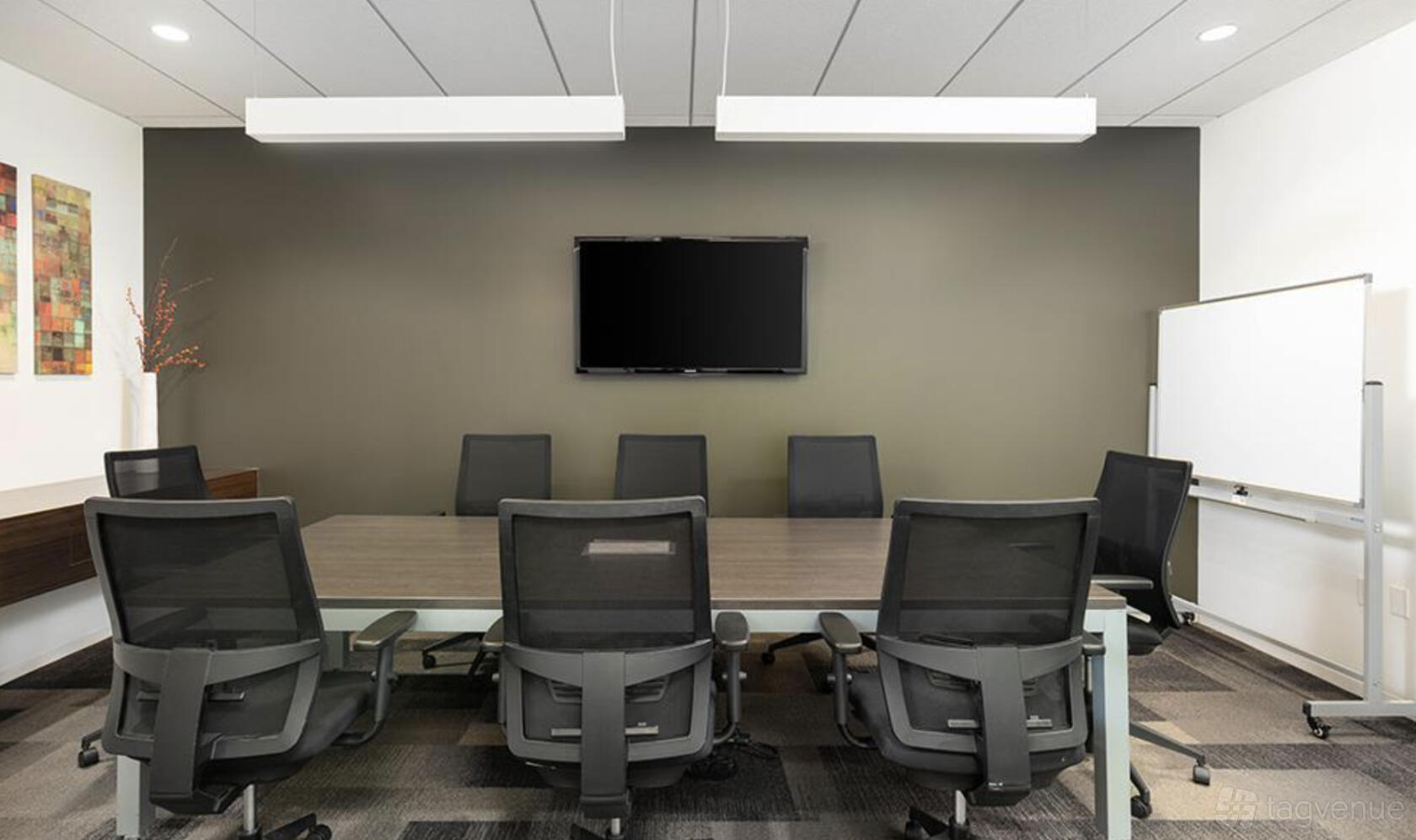 A meeting room with a long conference table, black mesh chairs, wall-mounted TV, and whiteboard at Premier Workspaces - La Jolla.