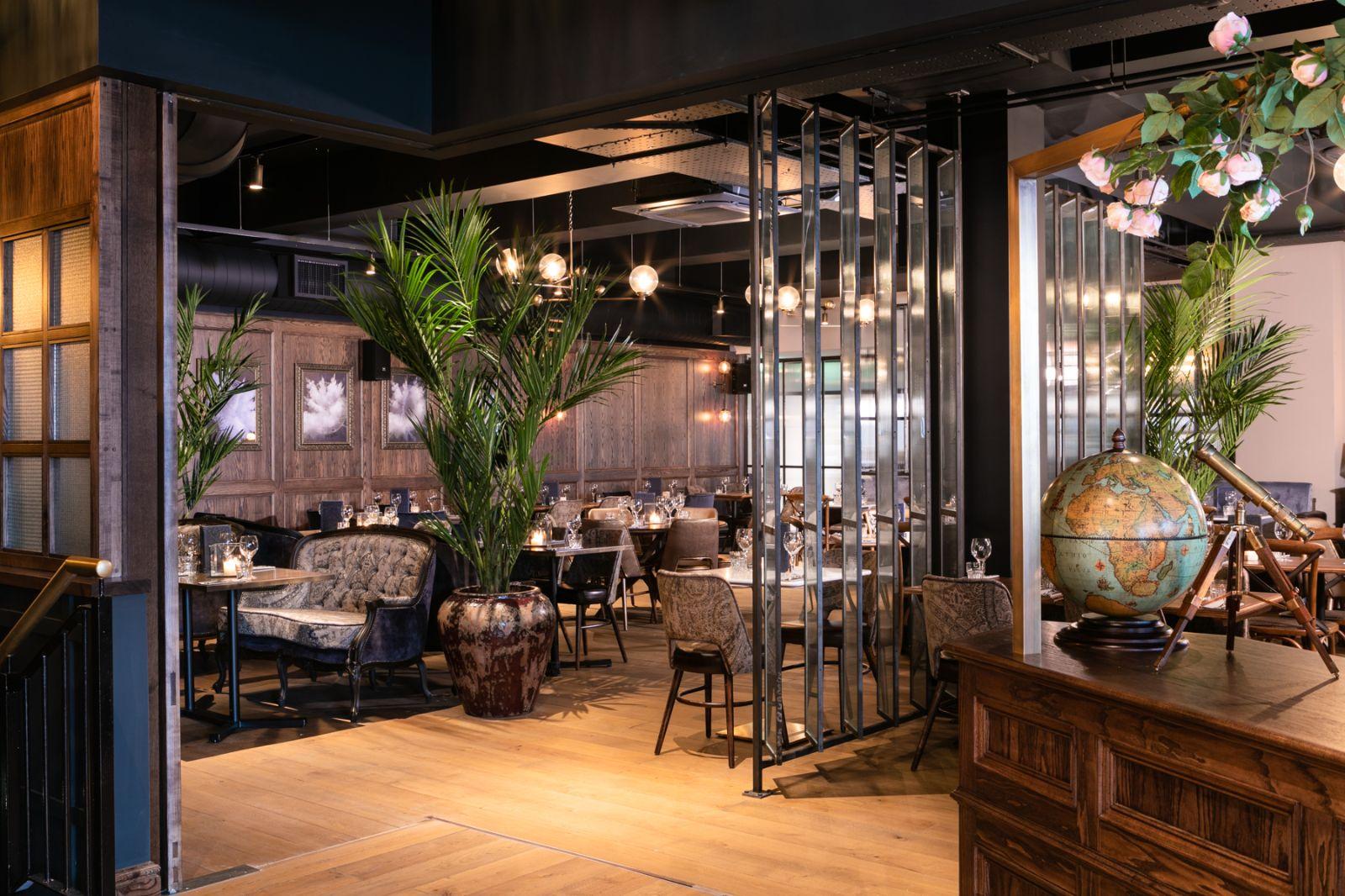 A restaurant with plush seating, potted palm plants, wood floors, and globe decor at The Lost & Found Bristol.