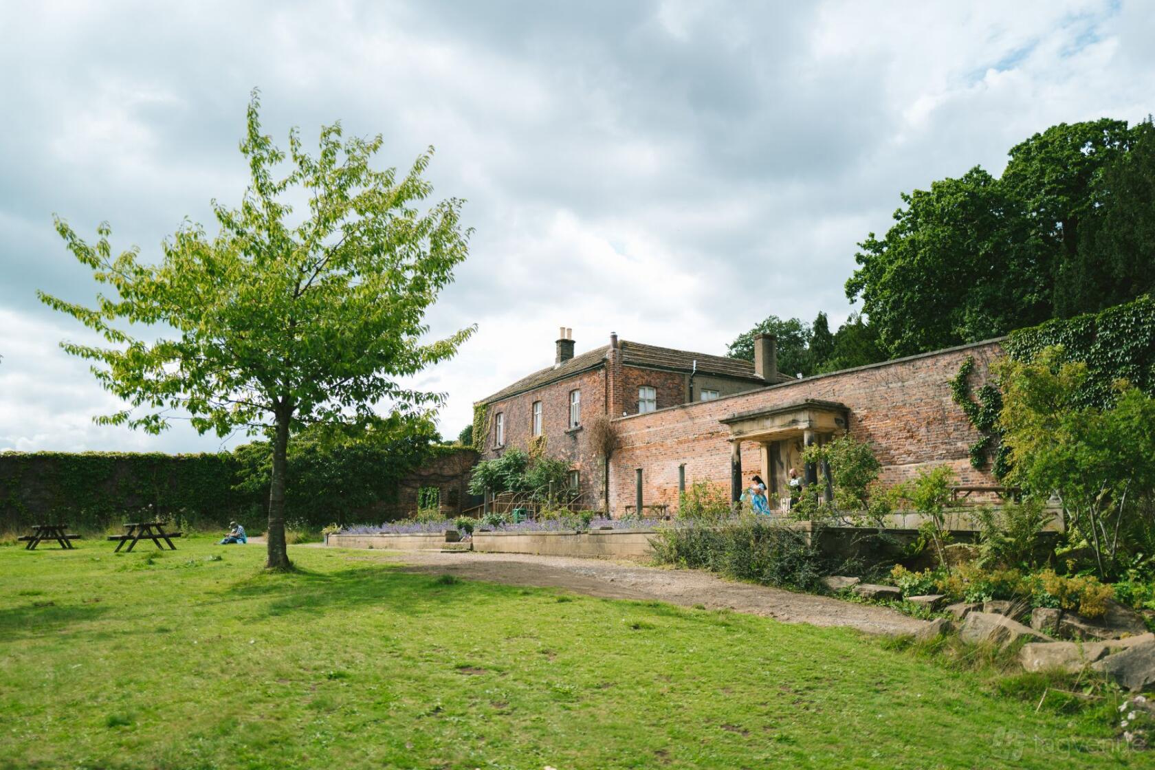 A country house meeting room with a brick exterior, garden lawn, and picnic benches at Harewood House.