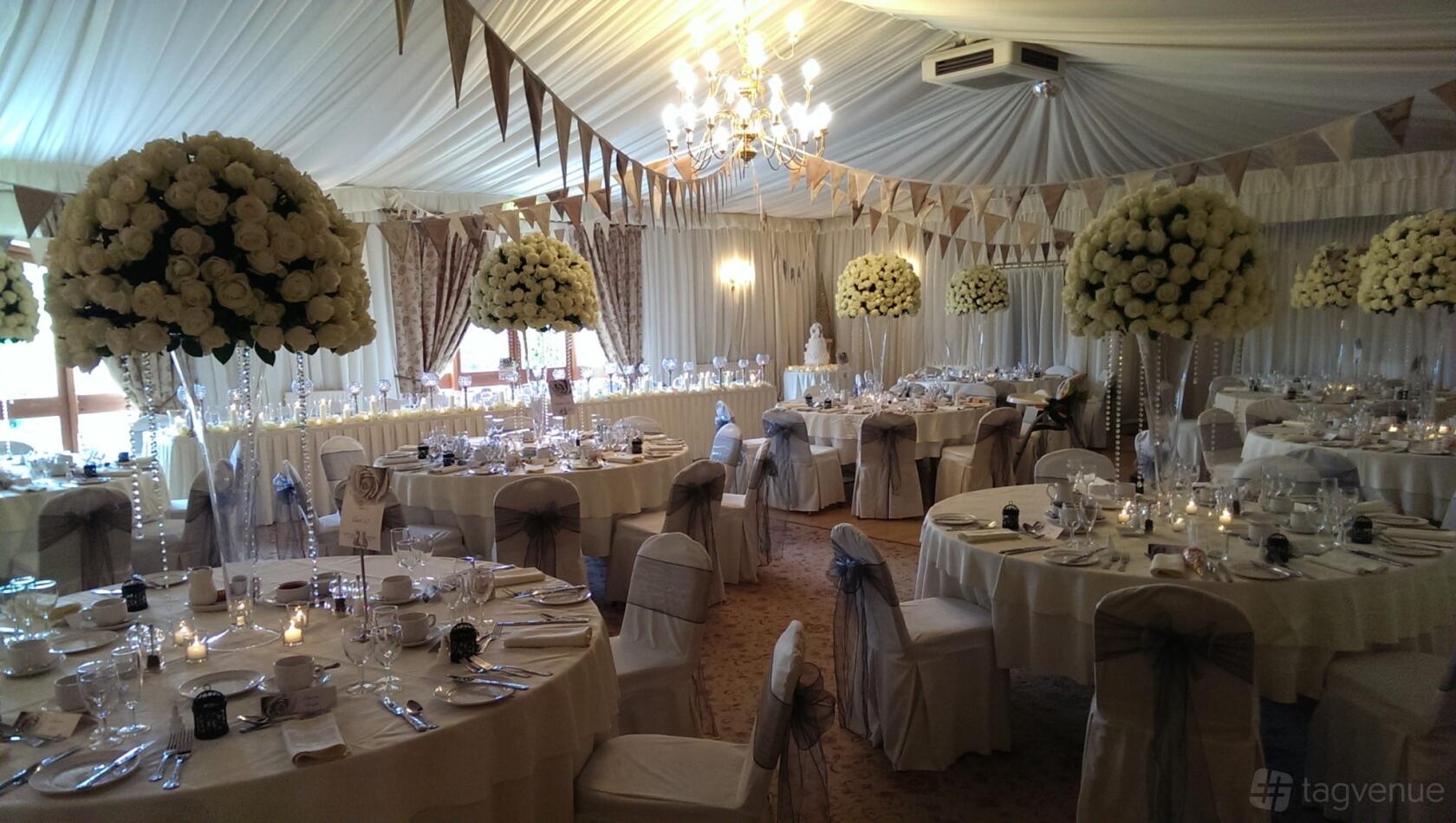 An event space in a hotel with chandeliers, round tables set with white linens, and tall floral centerpieces at Albright Hussey Manor